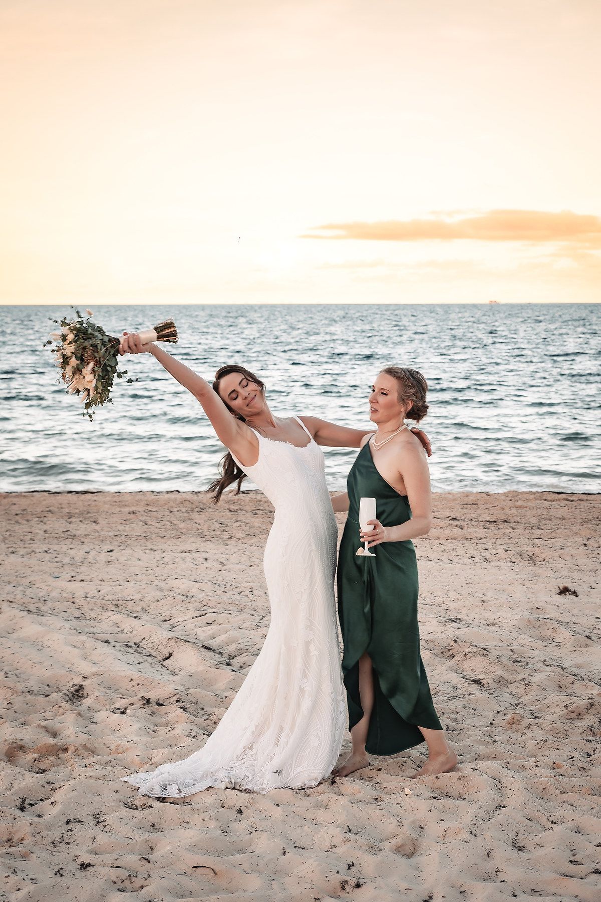 Wedding couple celebrates playfully on the beach during sunset.