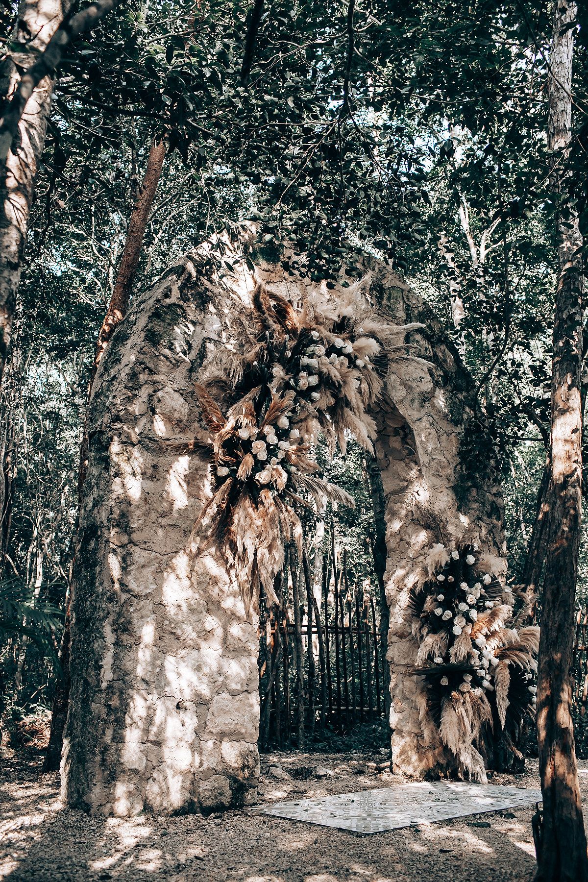 A rustic stone archway adorned with floral arrangements stands in a serene forest setting.