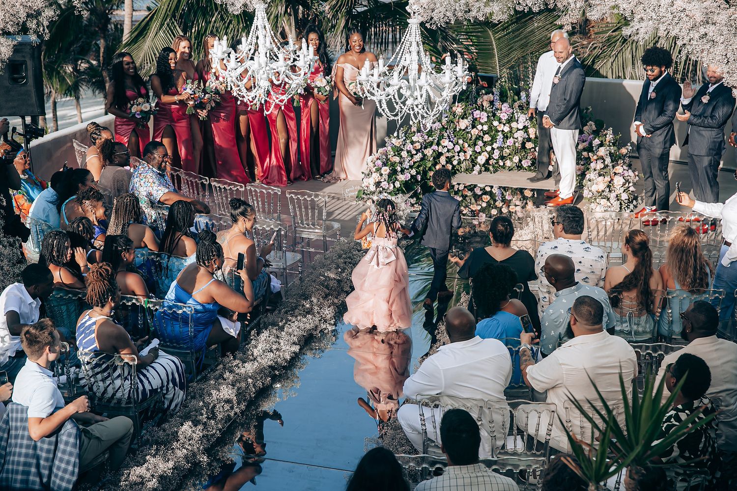 An elegant wedding ceremony with burgundy bridesmaids and white floral decor under crystal chandeliers.