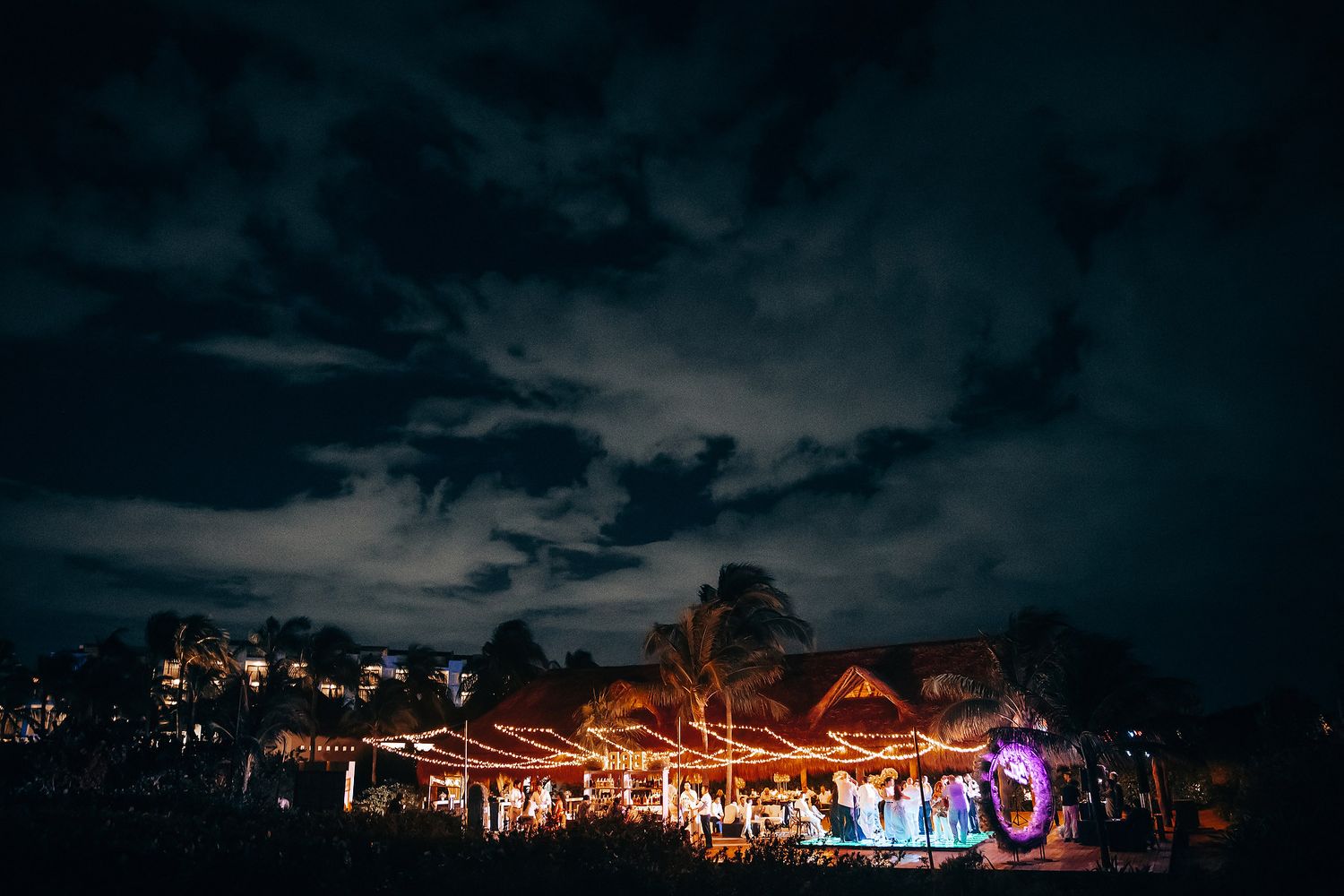 Nighttime wedding reception venue glows with warm lights under dramatic dark sky.