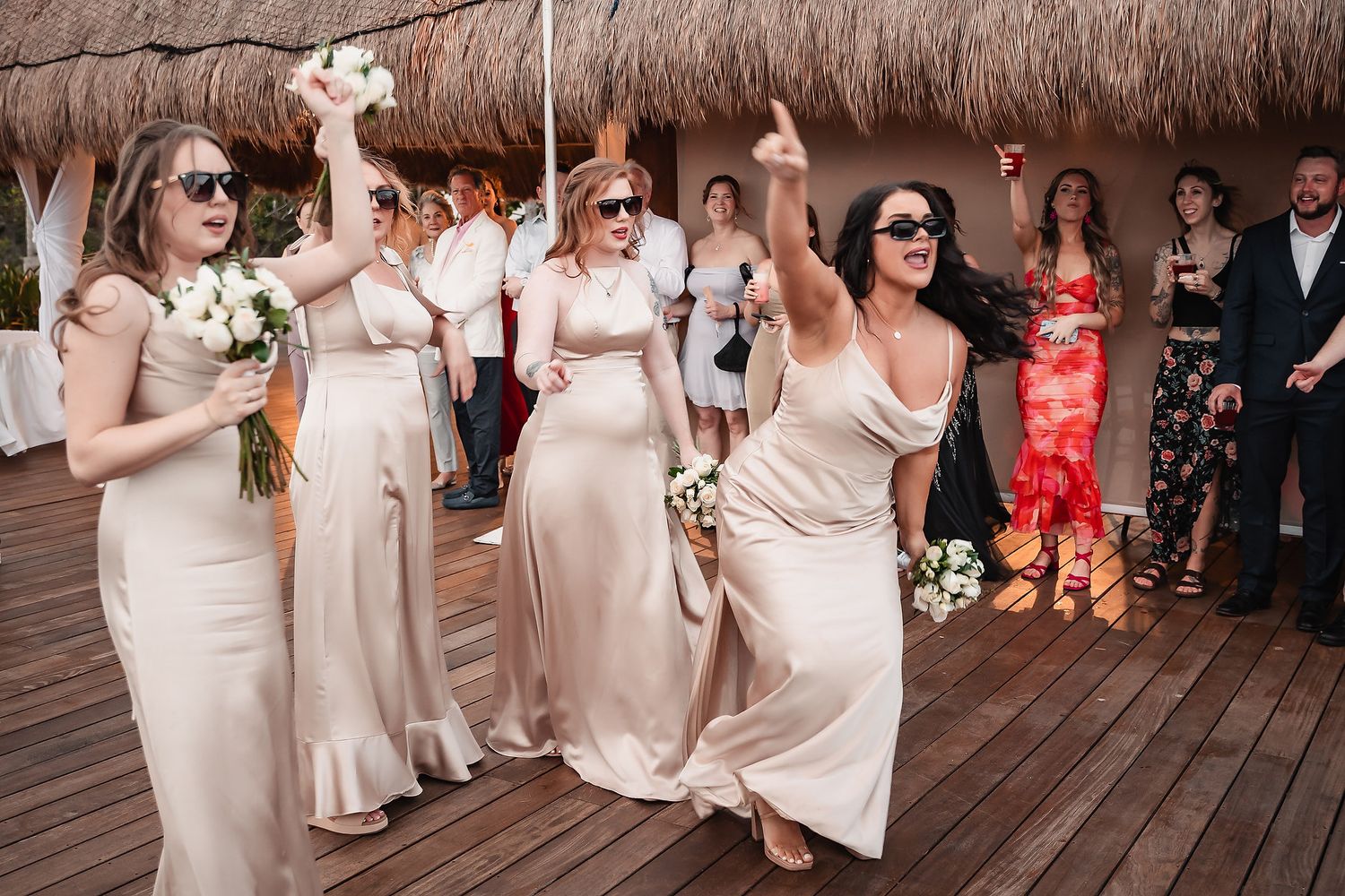Bridesmaids in blush pink dresses dancing together at an elegant wedding reception.