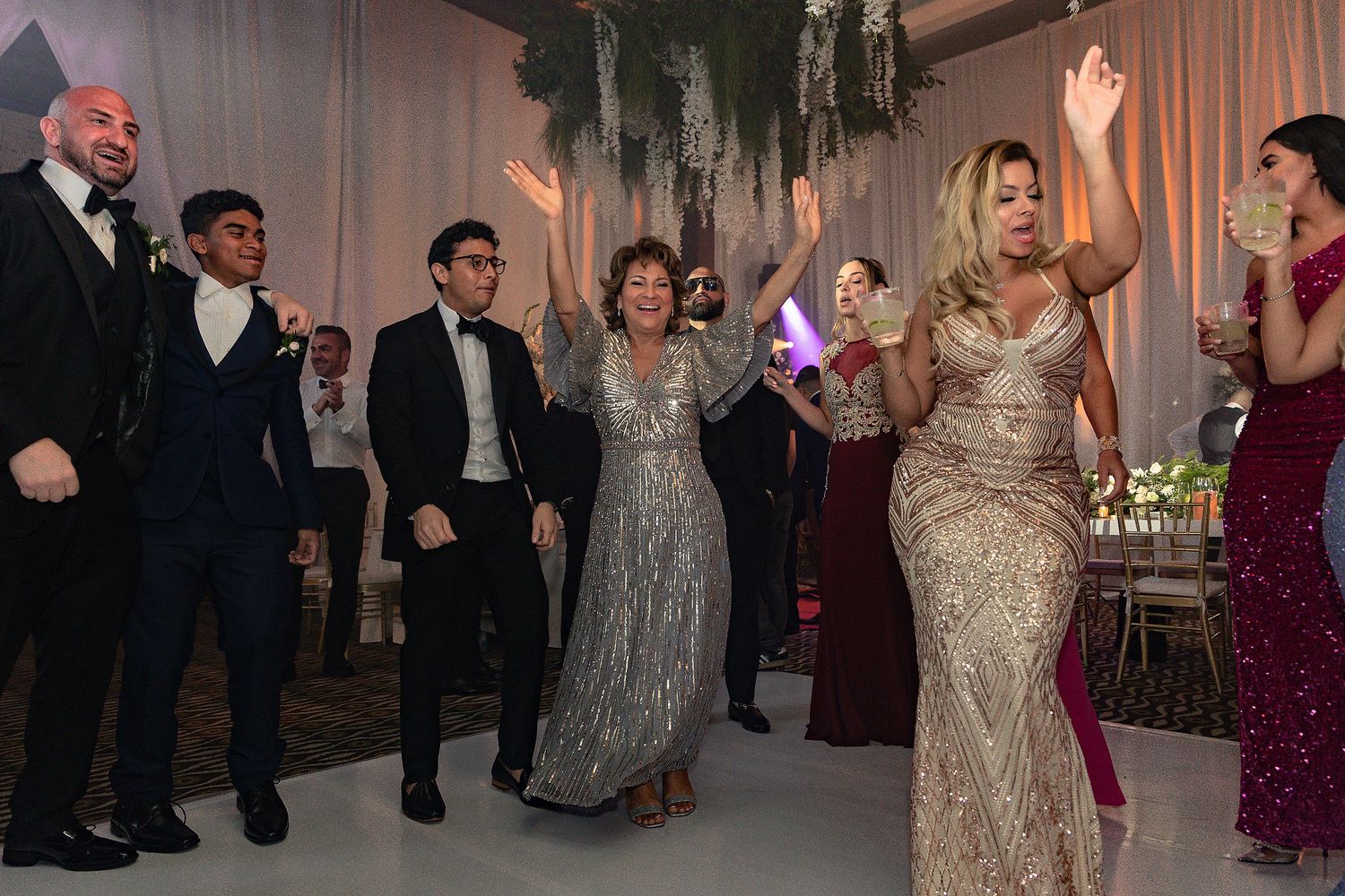 Wedding celebration with guests dancing beneath elegant draping and chandeliers at an indoor venue.