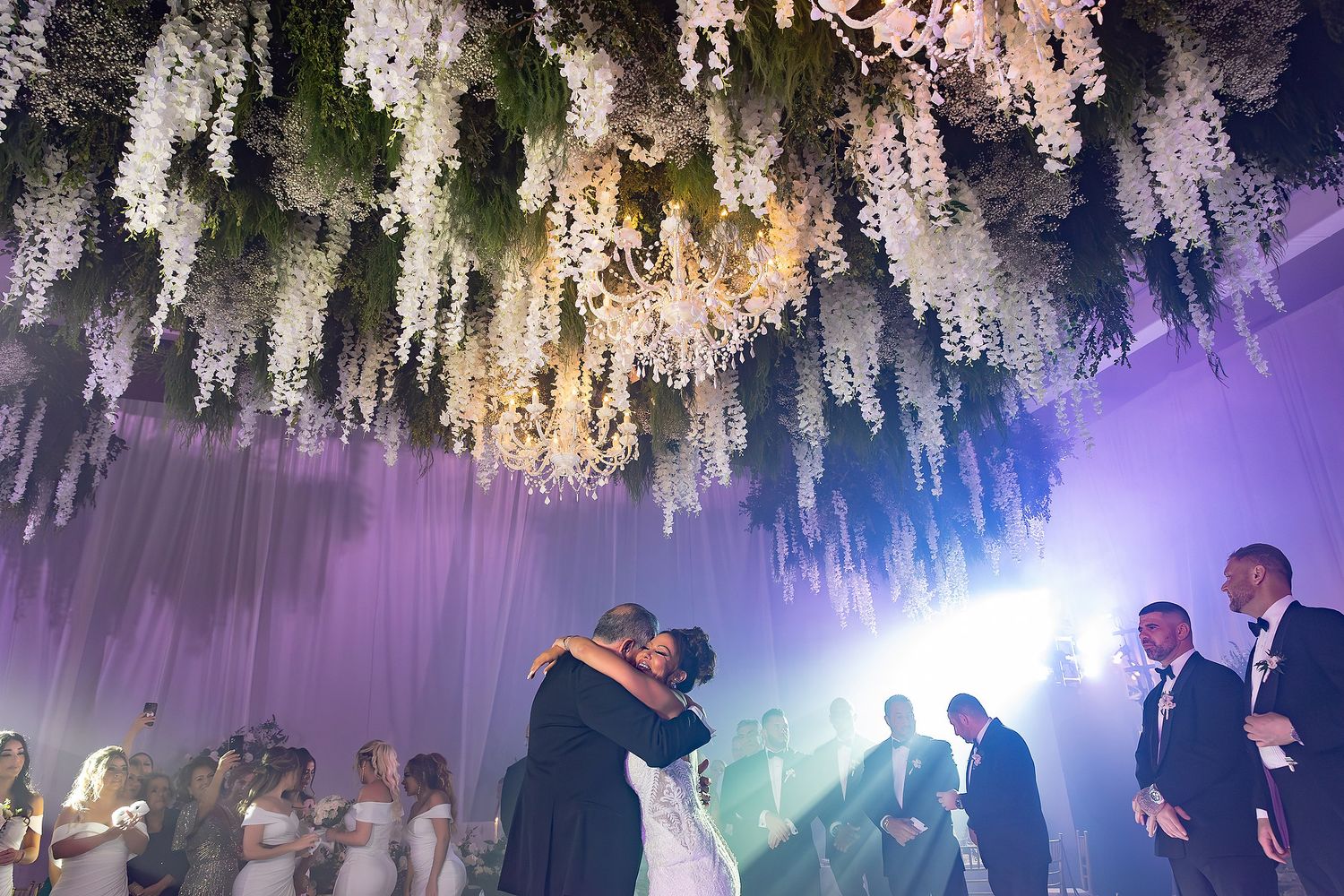 Elegant wedding venue with hanging crystal chandeliers and dancing silhouettes in purple and blue lighting.
