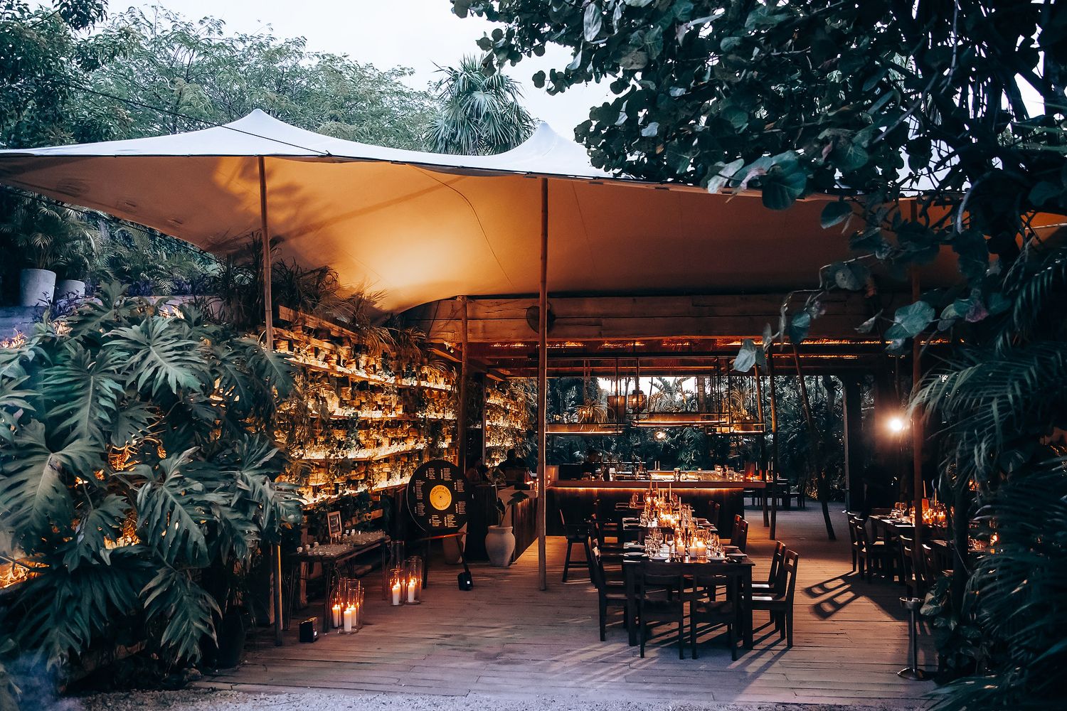 Outdoor wedding reception space with white canopy and wooden dining tables.