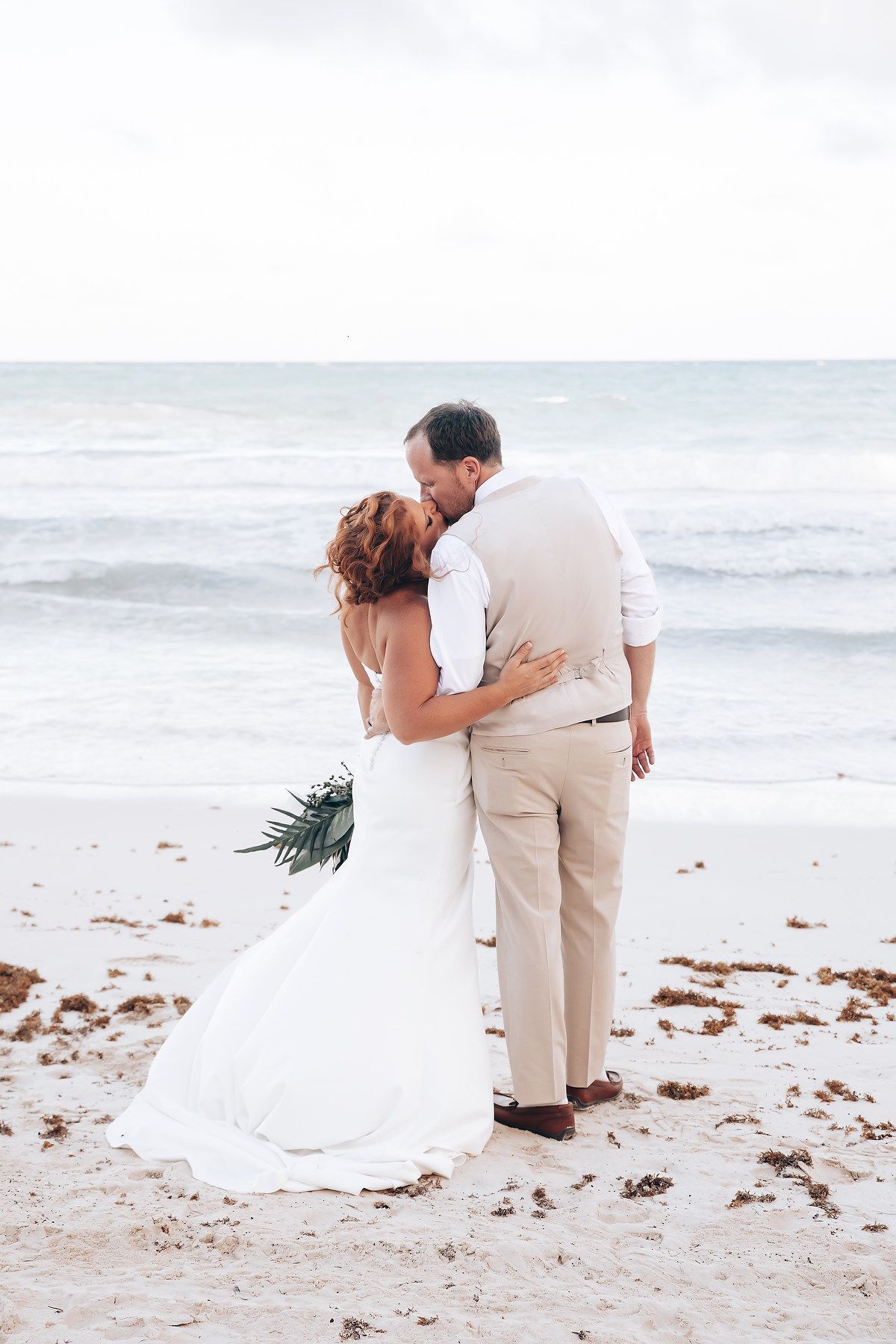 Intimate beachside moment captured with flowing white dress against the ocean backdrop.