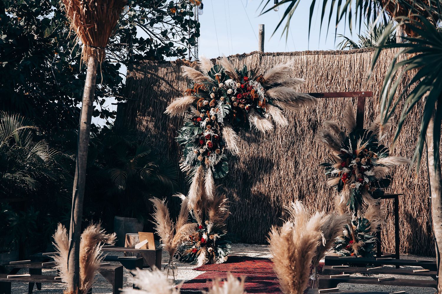 Boho wedding aisle decorated with pampas grass and palm fronds under string lights.