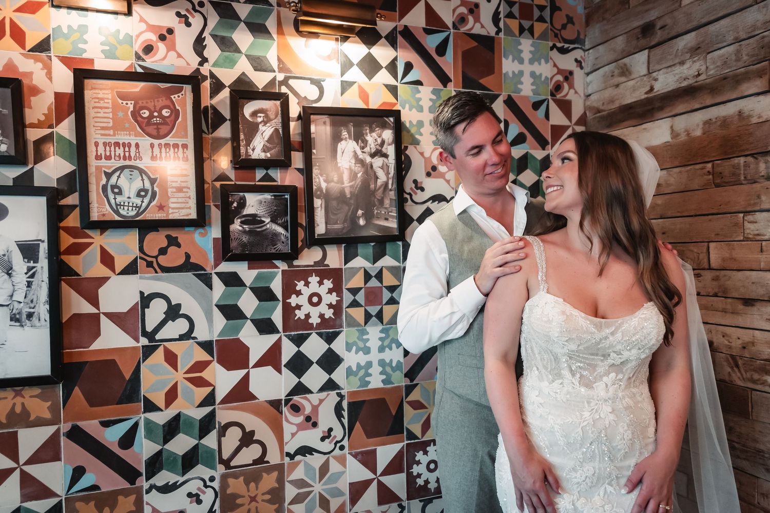 Wedding couple poses against rustic brick wall with decorative geometric tile patterns.