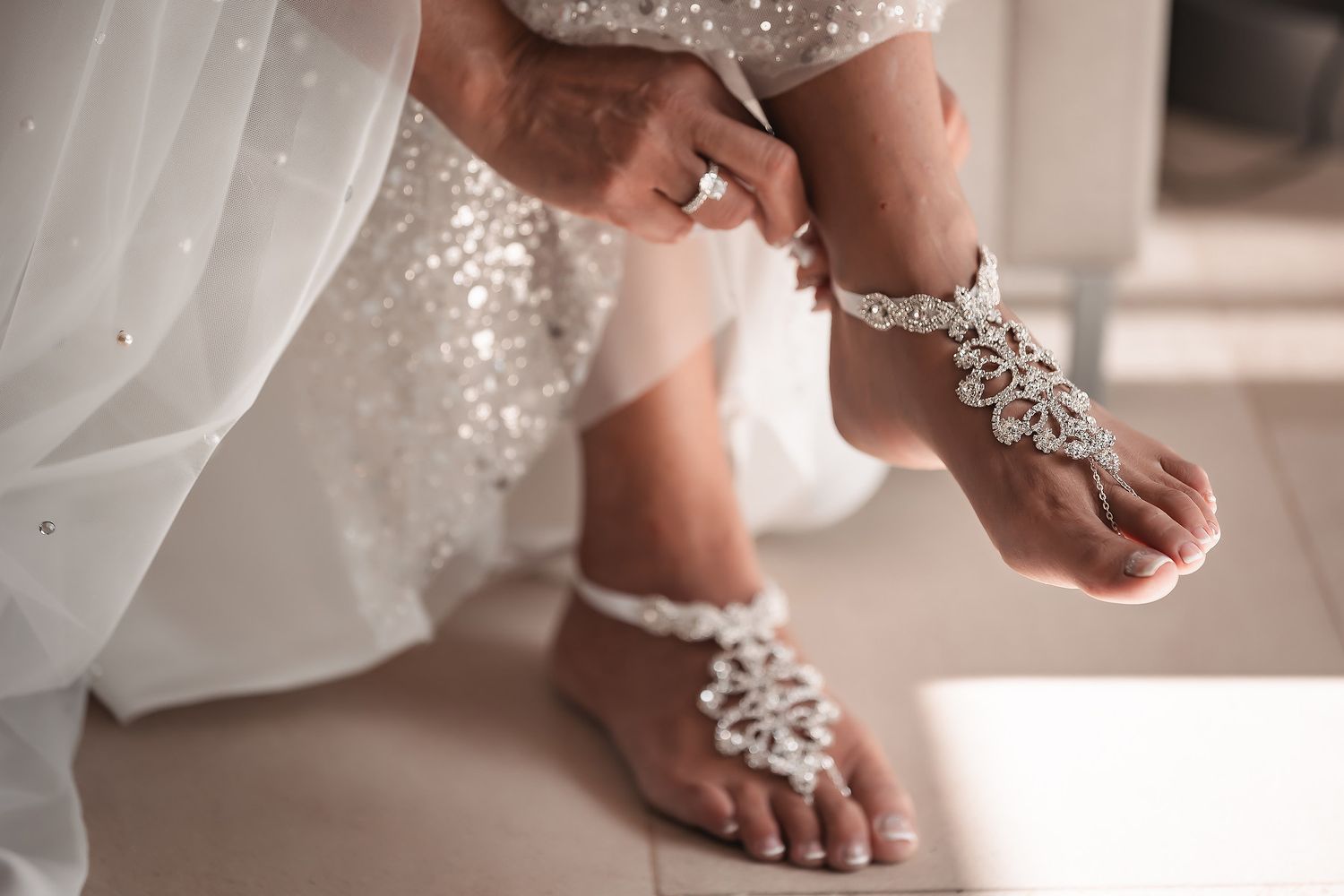 Close-up detail of sparkly bridal shoes and flowing white dress hem on a wooden floor.