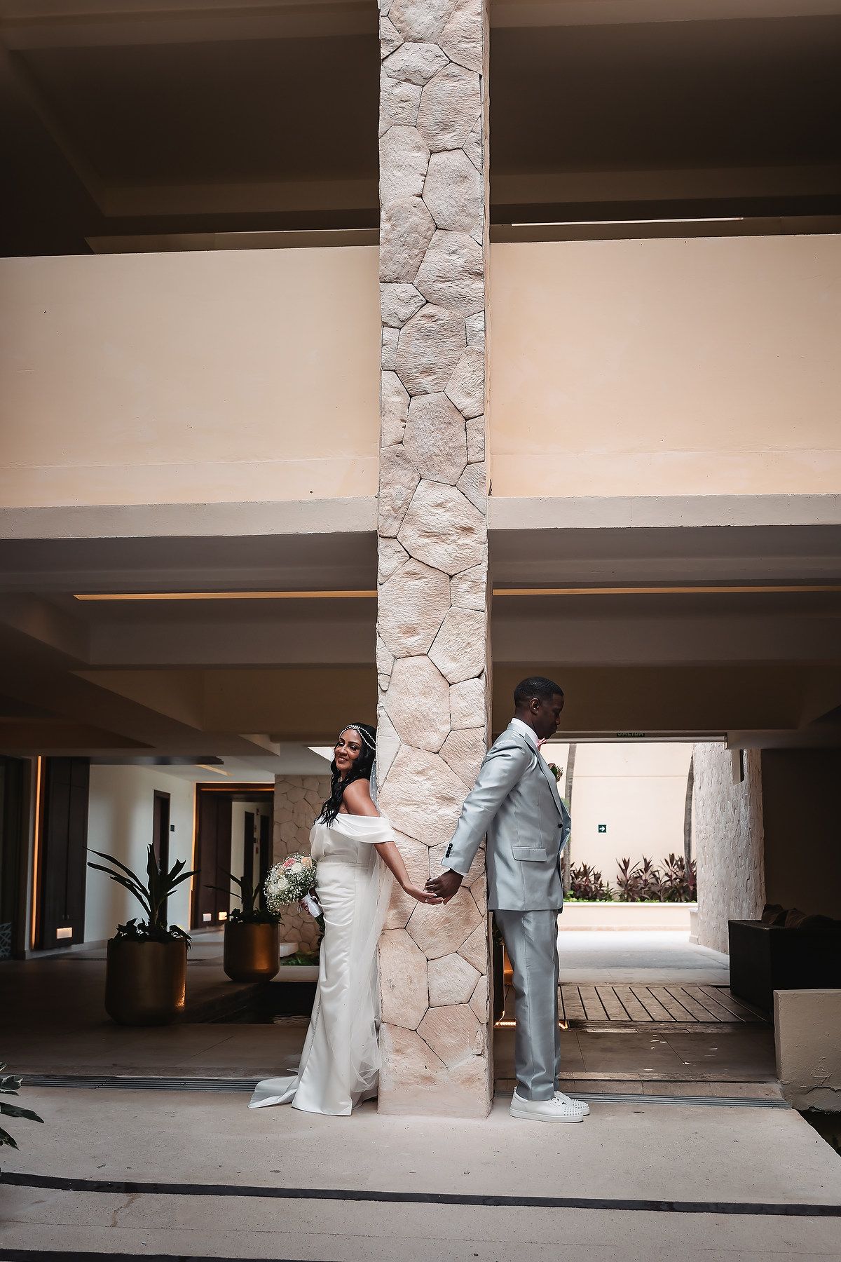 Wedding couple sharing a first look moment behind stone pillars in an indoor venue.