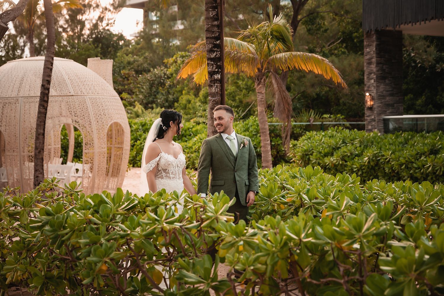Wedding couple walking through a lush tropical garden path with palm trees.