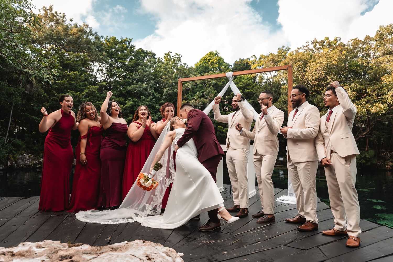 Bridal party in burgundy and beige attire poses on stone pathway during outdoor autumn wedding.