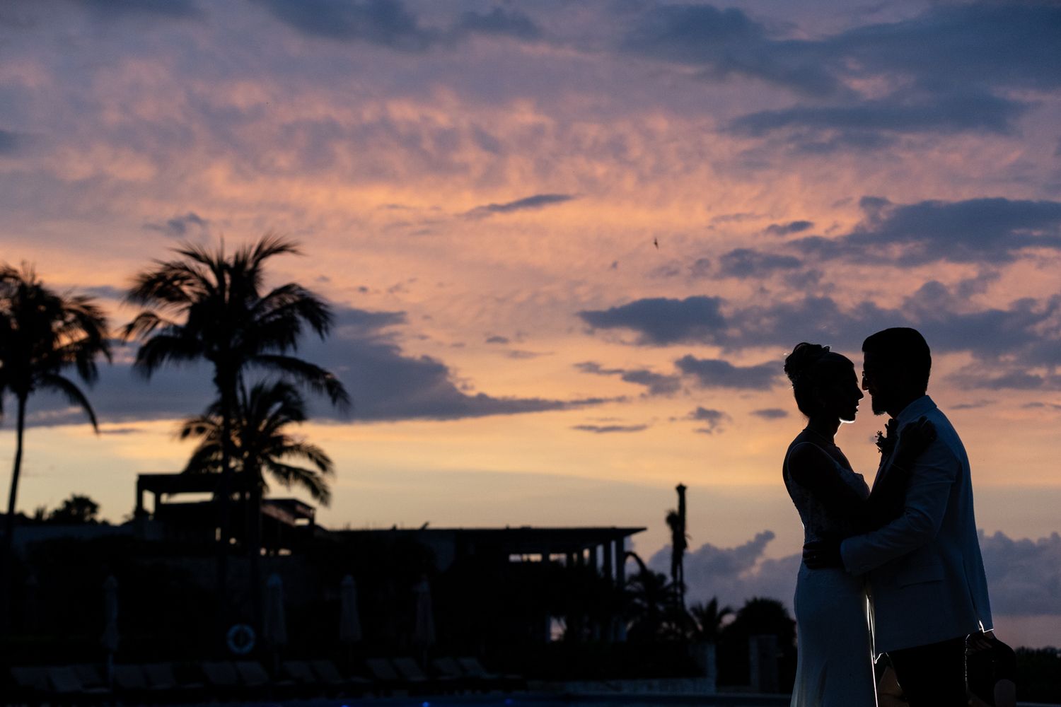 Silhouette of a romantic couple embracing at sunset on a tropical beach with vibrant purple and pink skies.