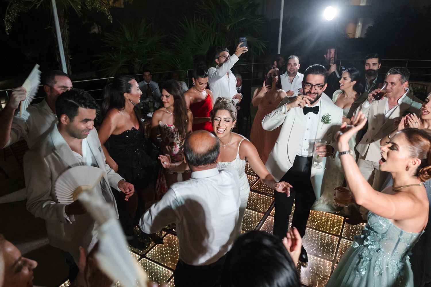Joyful wedding reception guests dancing and celebrating together at an elegant outdoor evening party.