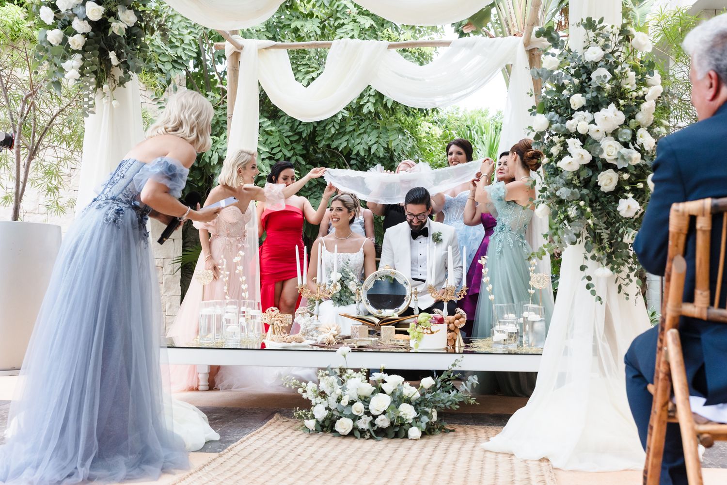 Elegant outdoor wedding ceremony with couple at decorated altar, surrounded by bridesmaids and floral arrangements.
