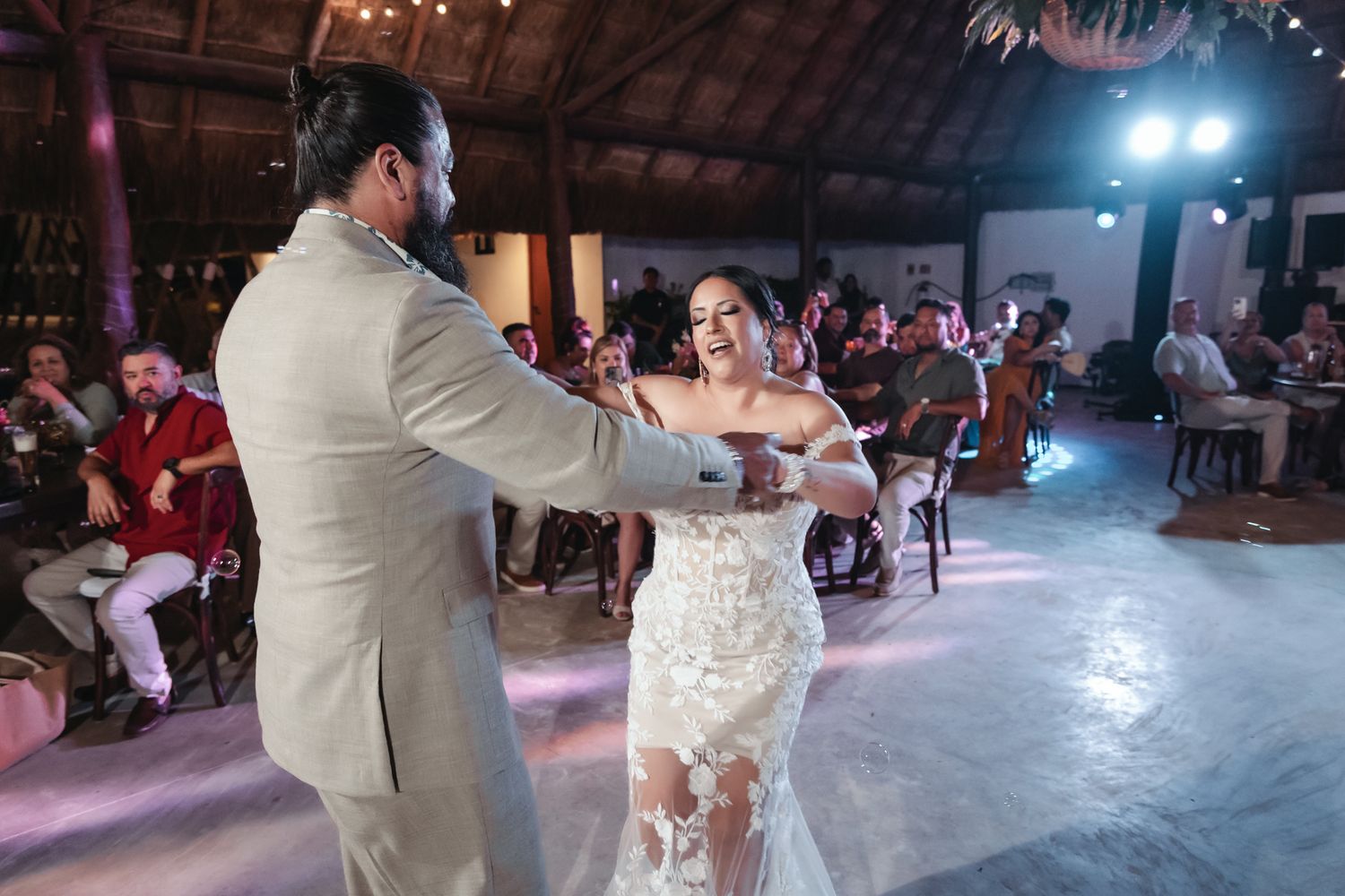 Bride and groom share their first dance at a romantic wedding reception in a rustic tropical venue.