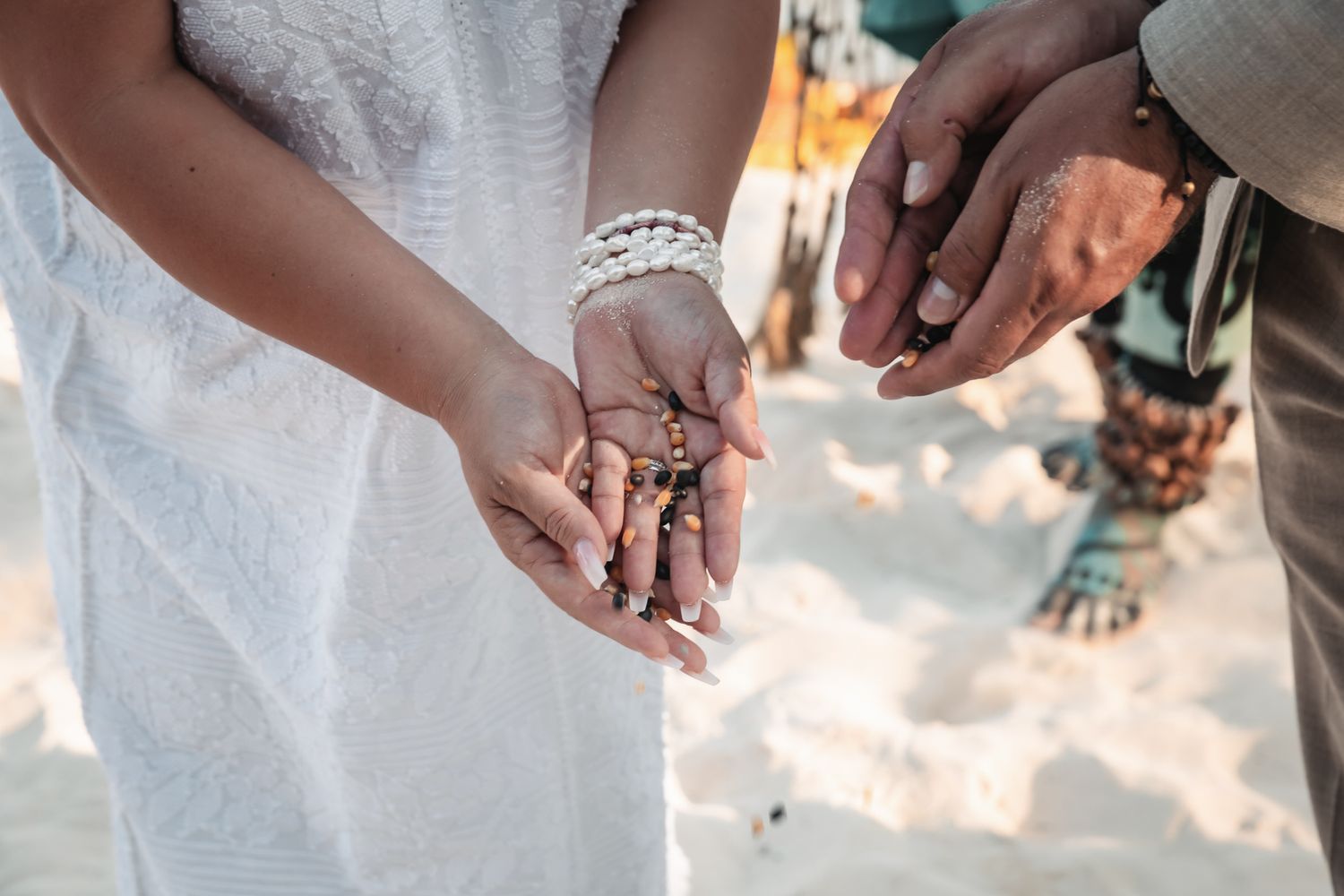 Couple holding rosary beads during a beach wedding ceremony, bride in white dress with pearl bracelet.