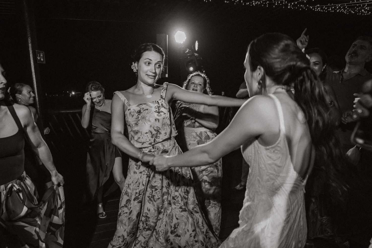 Two women dance joyfully at a wedding reception in this black and white photo.