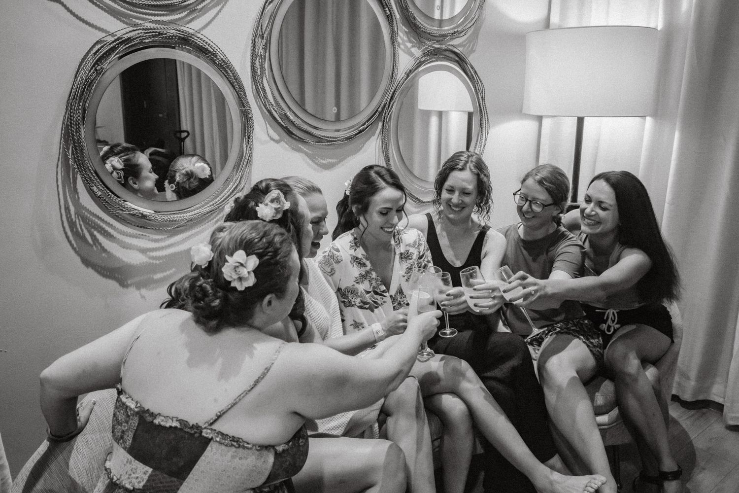 Black and white photo of bride and bridesmaids toasting with champagne glasses while getting ready together.
