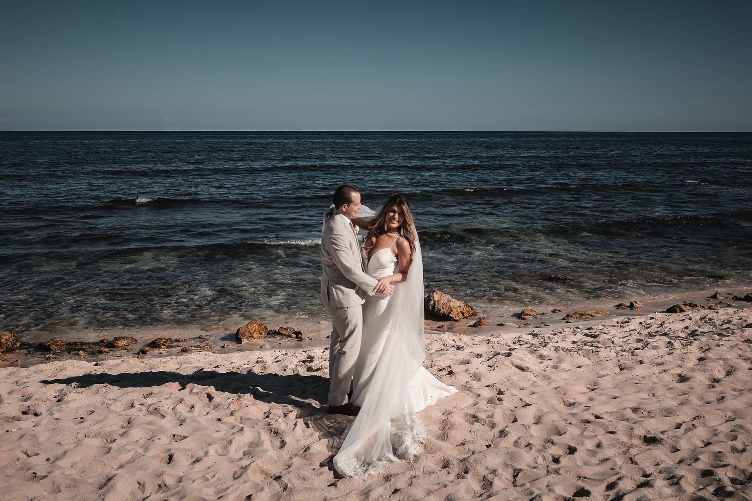 Bride and groom sharing a romantic moment on a sunny sandy beach by the sea on their wedding day.