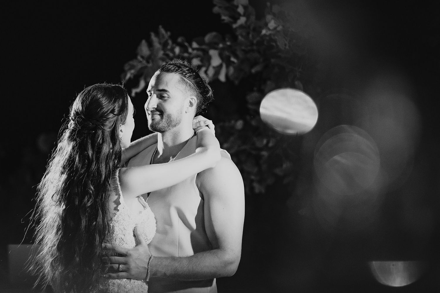 Black and white photo of a couple embracing and smiling at each other outdoors at night.