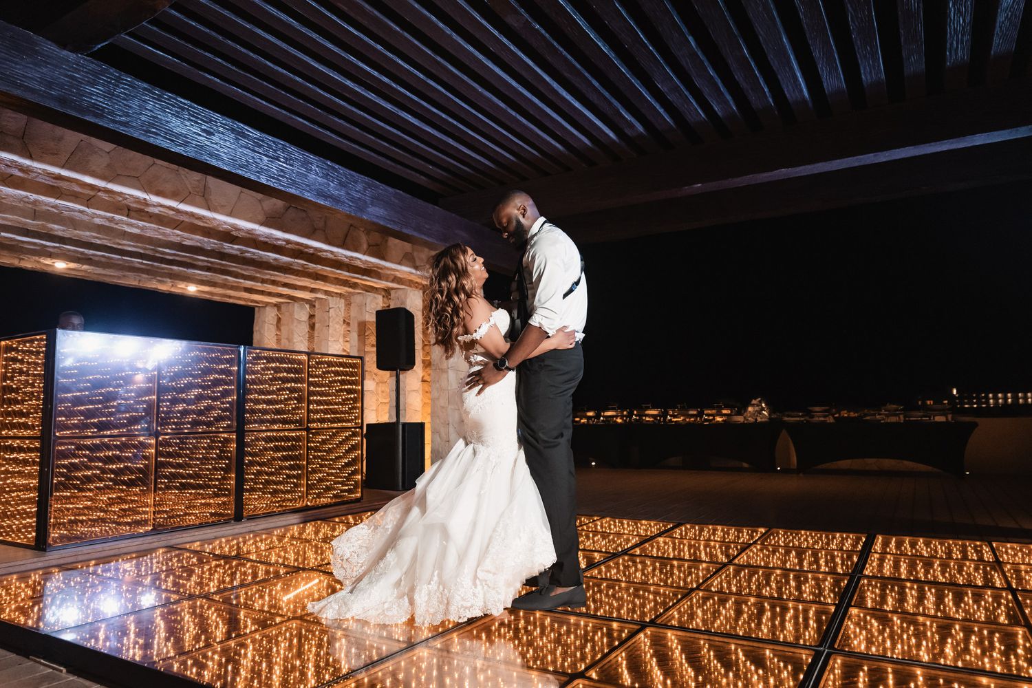 Bride and groom share romantic first dance on illuminated floor at elegant outdoor night wedding reception.