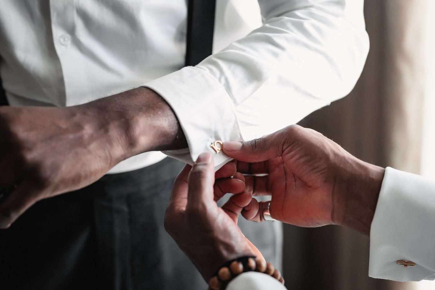 Groom having gold cufflinks fastened on white dress shirt sleeves before wedding ceremony.