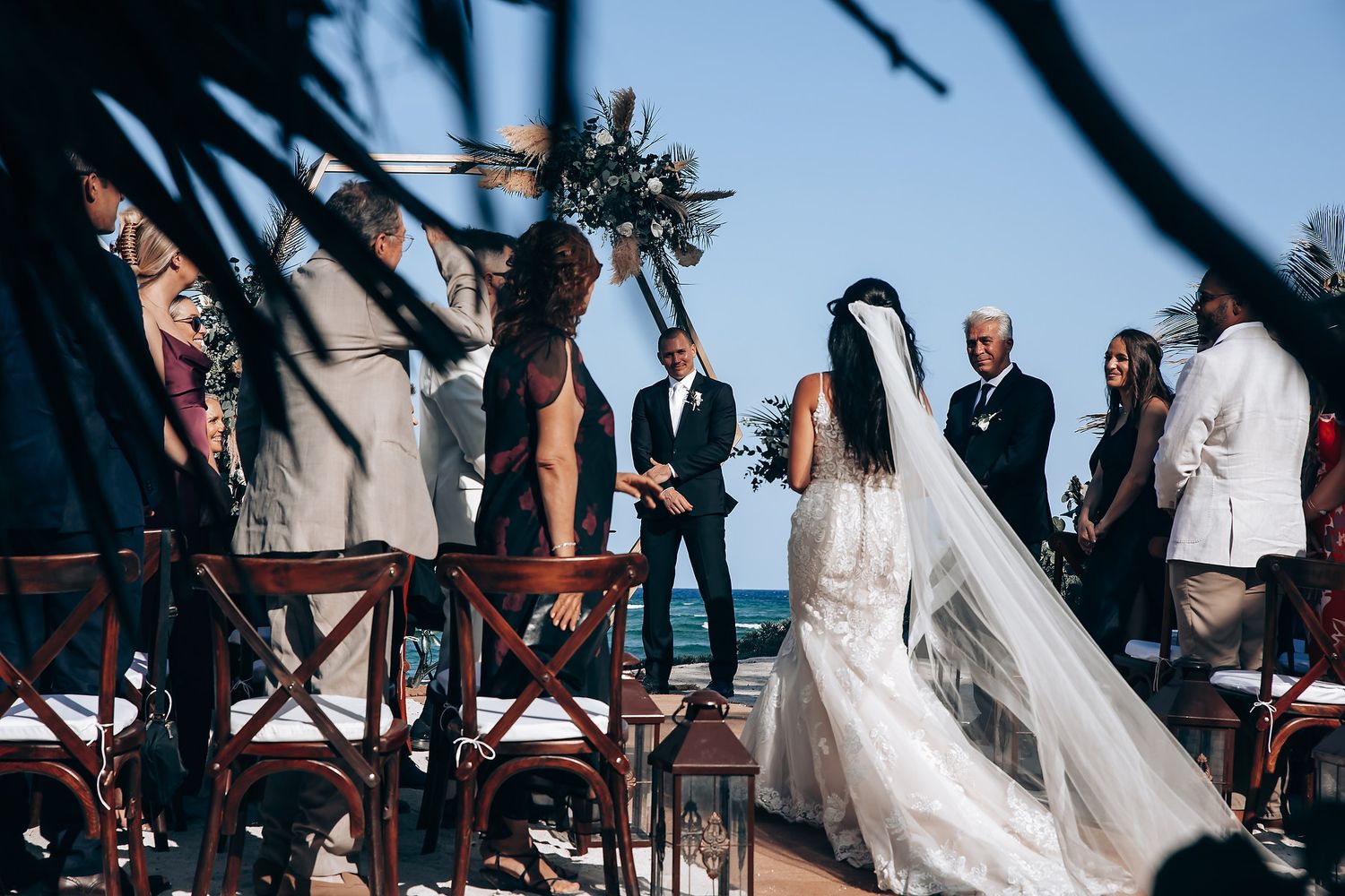 Oceanfront wedding ceremony setup with white chairs and flowing fabric decorations against blue waters.
