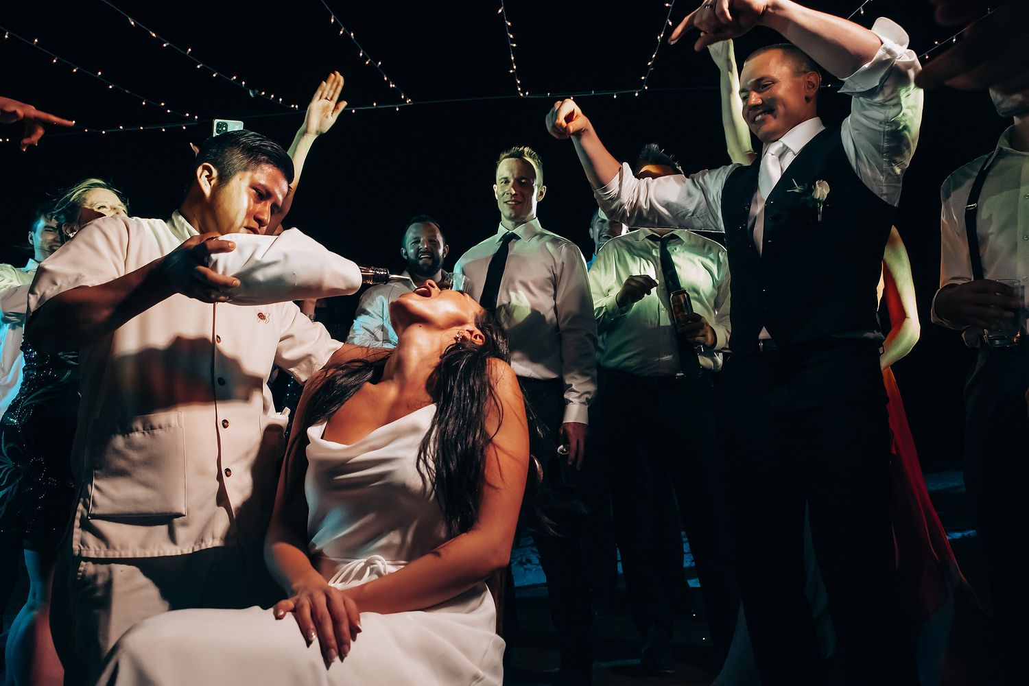 Wedding guests dancing under atmospheric lighting at an evening reception celebration.