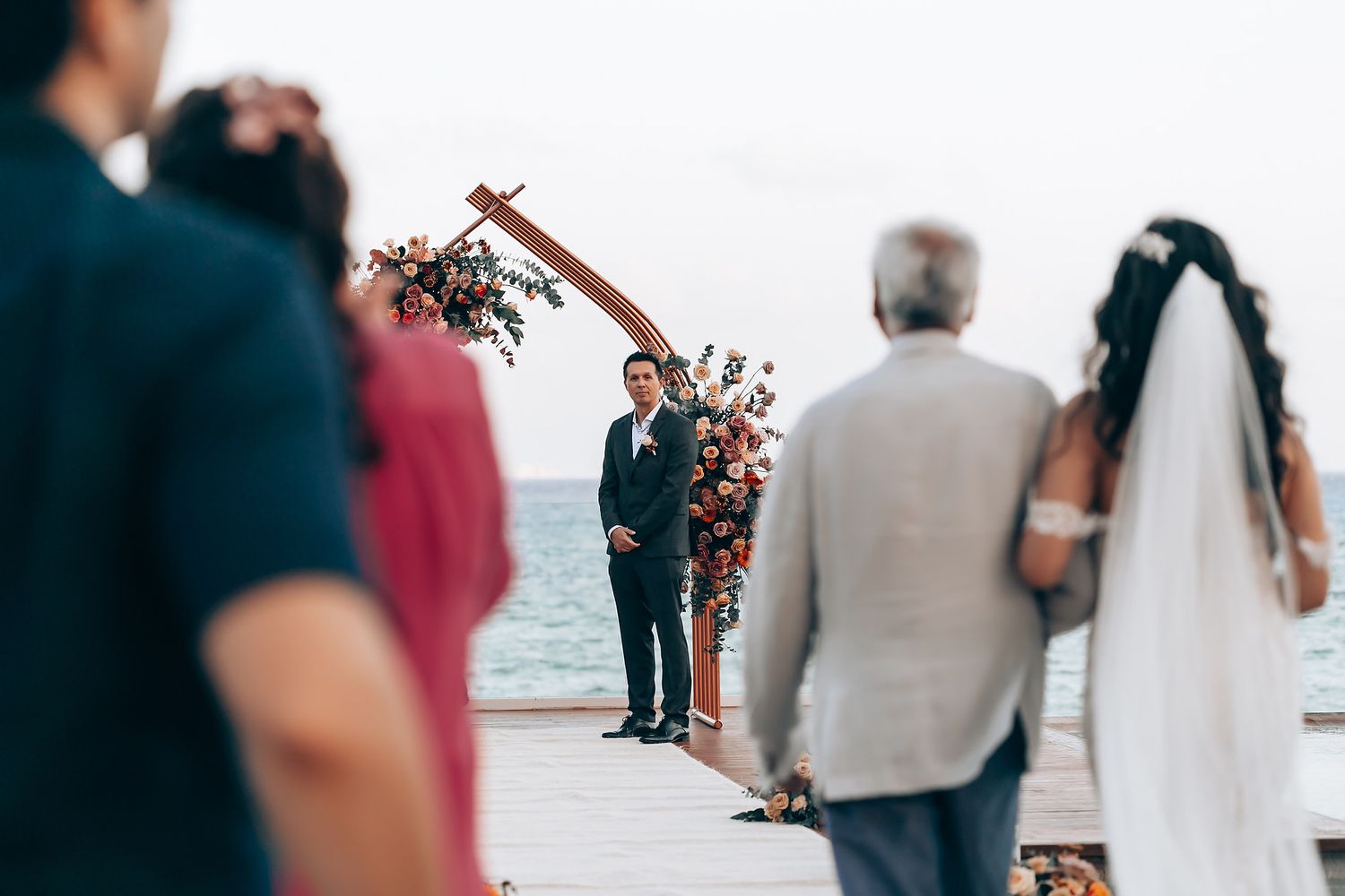 Intimate waterfront wedding ceremony with floral arch decorations and guests in attendance.