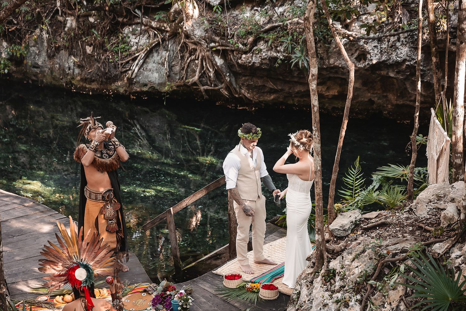 Couple exchanges vows at a cenote wedding ceremony in Mexico with a shaman officiant on a wooden deck.