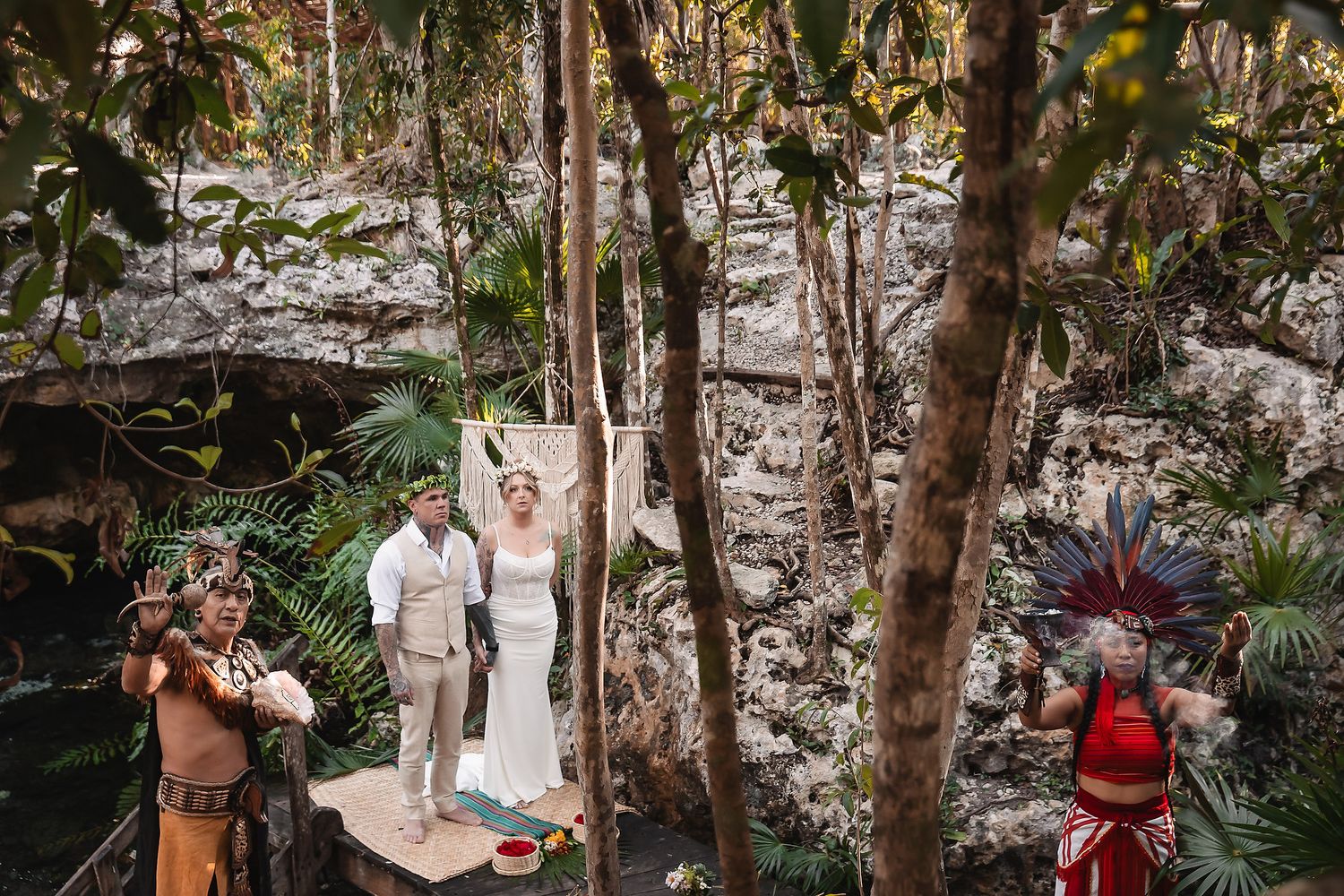 Couple exchanges vows in a lush jungle cenote ceremony with indigenous performers in traditional Mayan attire.