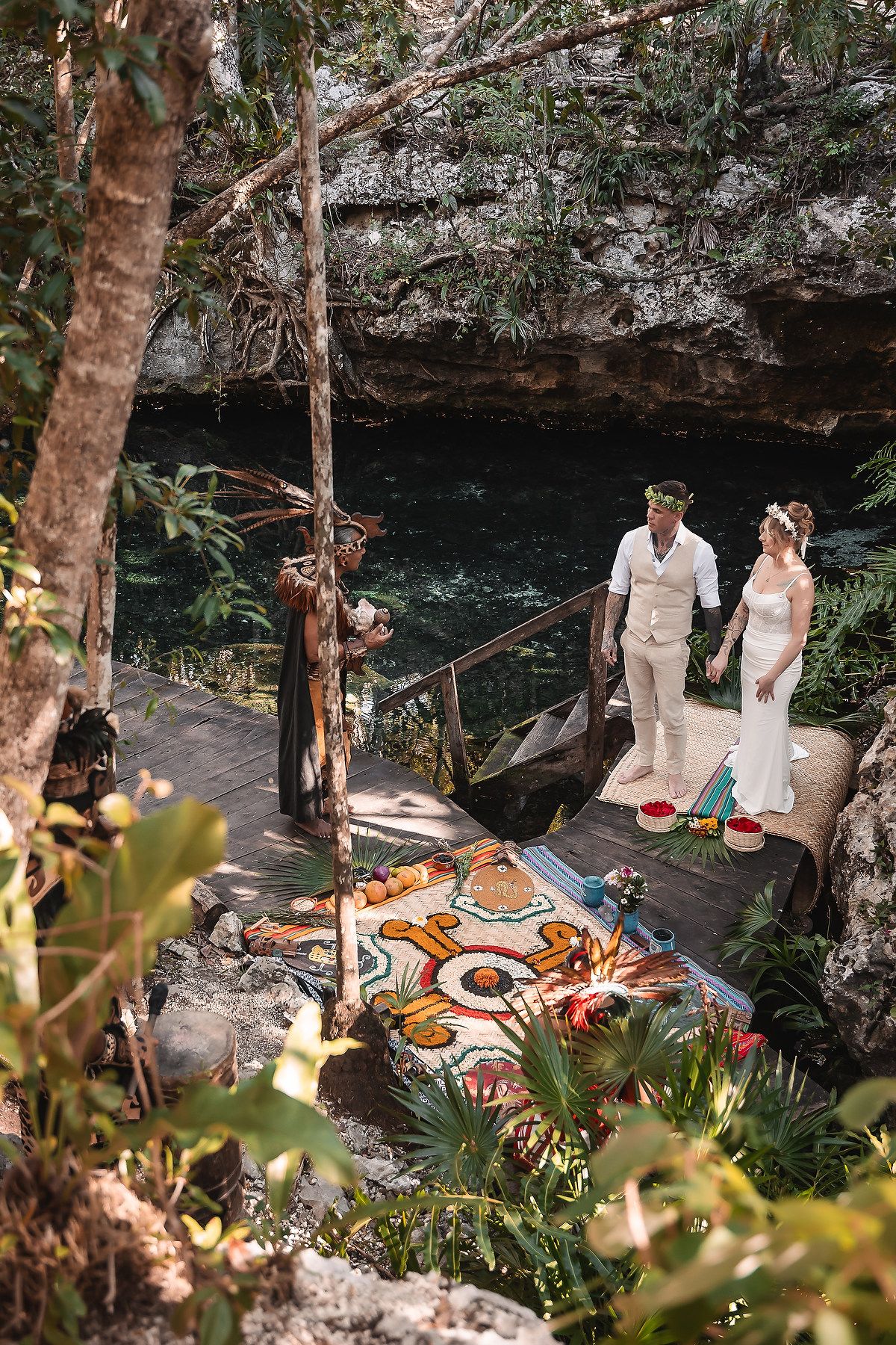 Couple exchanges vows at a cenote wedding ceremony in a lush jungle setting with colorful decor.