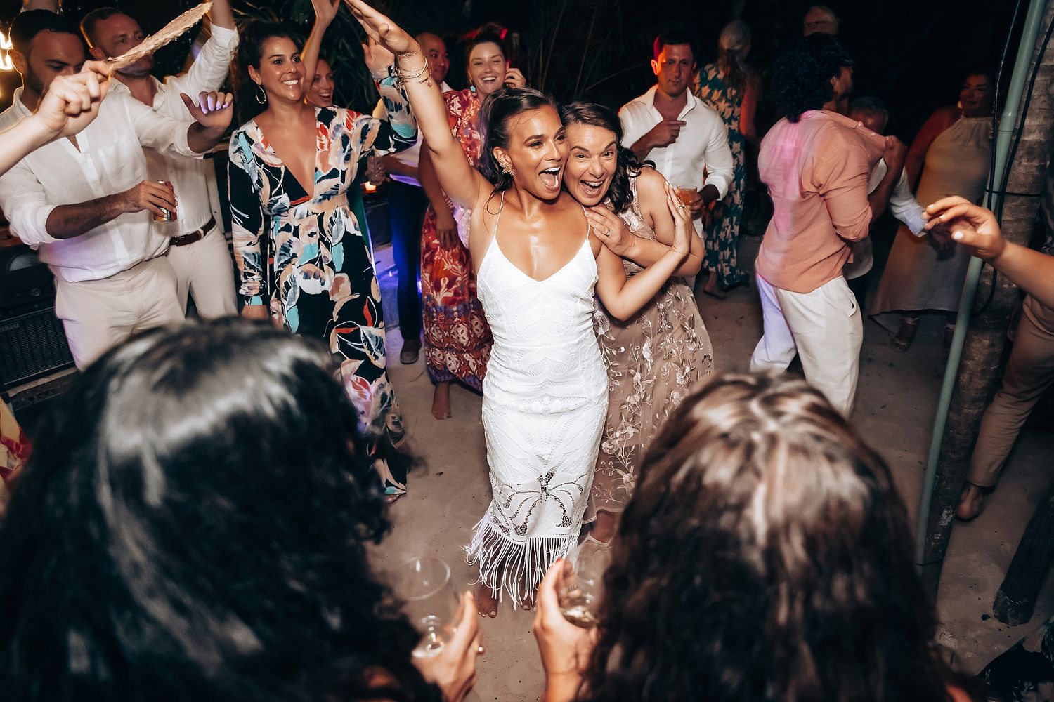 Guests dancing and celebrating at an evening beach wedding reception with festive lighting.