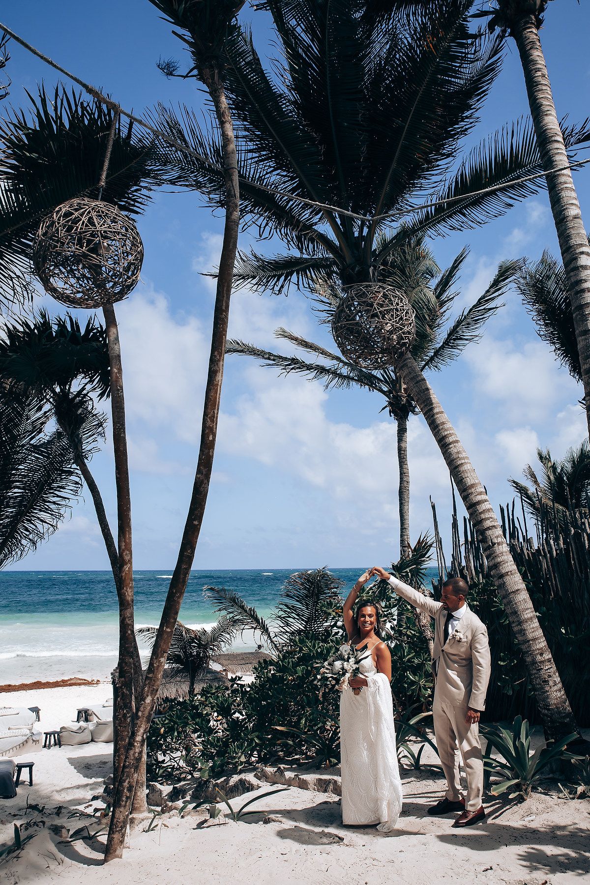 A tropical beach wedding ceremony setup with palm trees swaying over white sand and turquoise waters in the background.