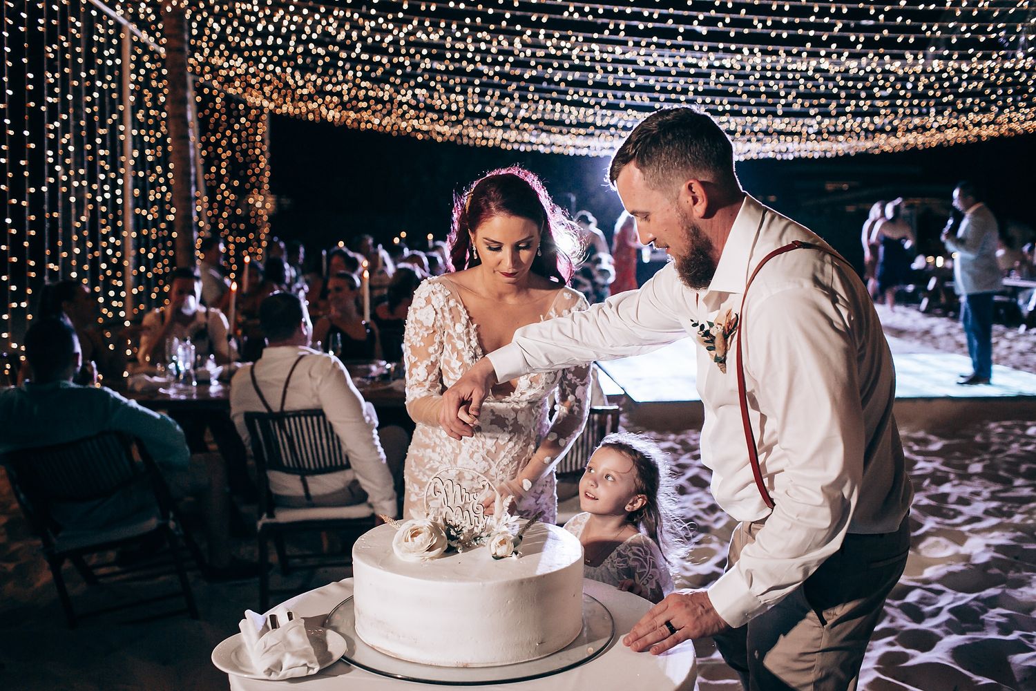 Wedding reception celebration with string lights and decorative cake cutting moment.