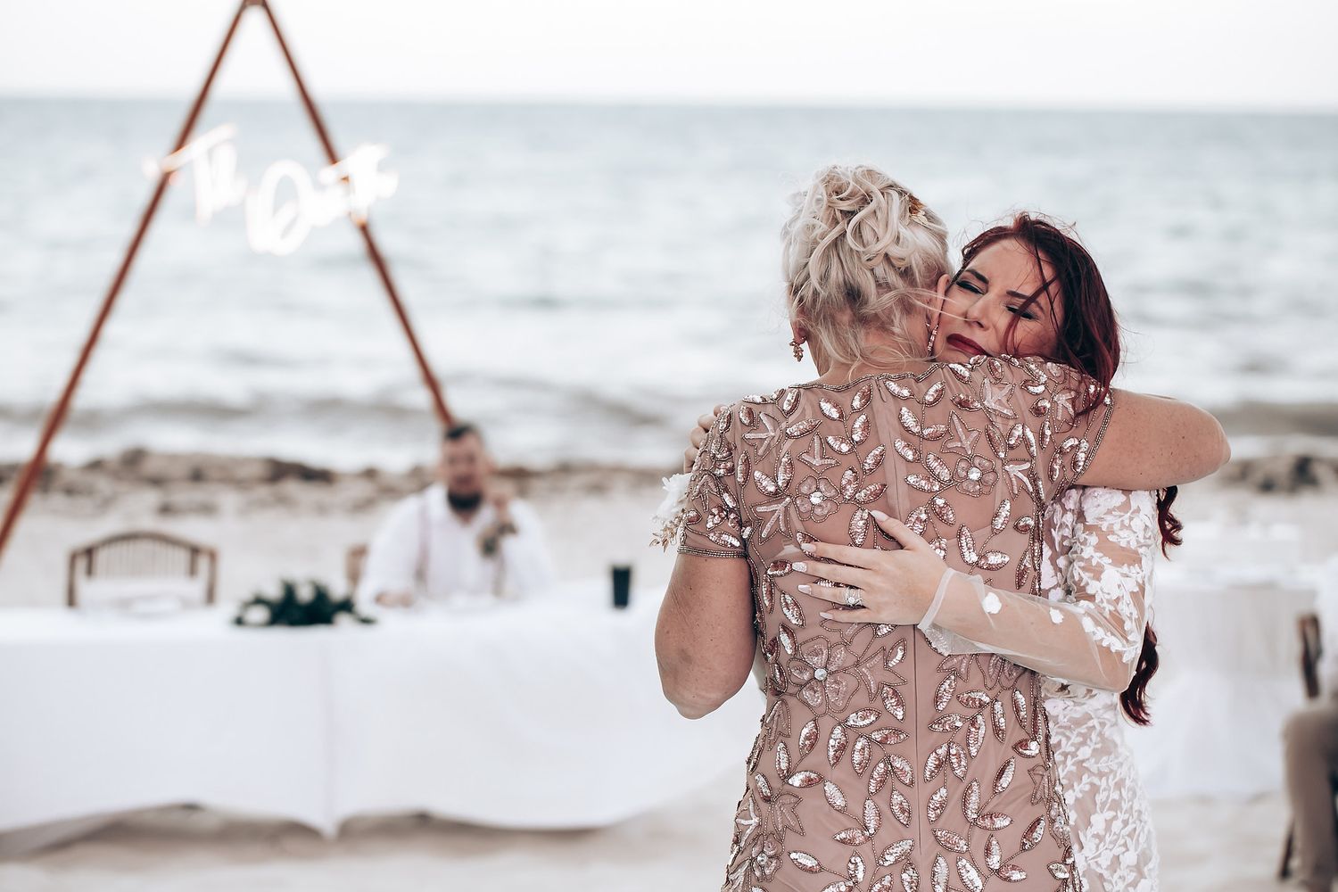 Romantic beach wedding setup with wooden A-frame arch decorated in floral arrangements.