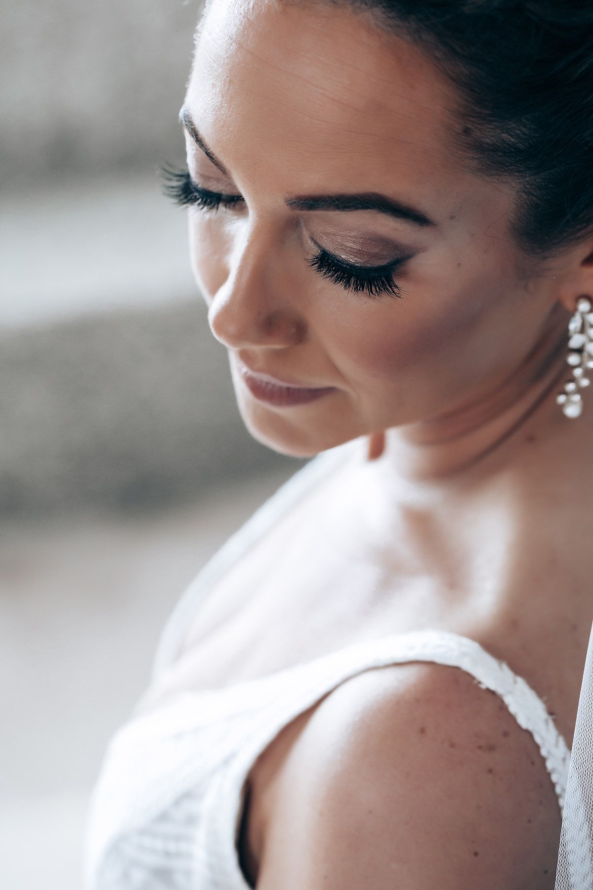 Close-up profile view of bridal makeup with dramatic eyelashes and sparkling earrings.