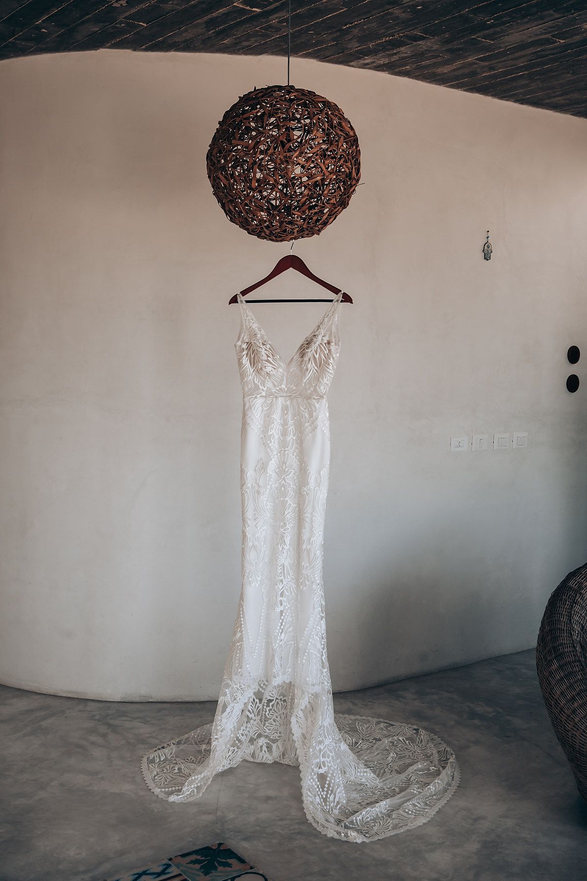White lace wedding dress hanging from rustic ceiling with decorative woven pendant light.