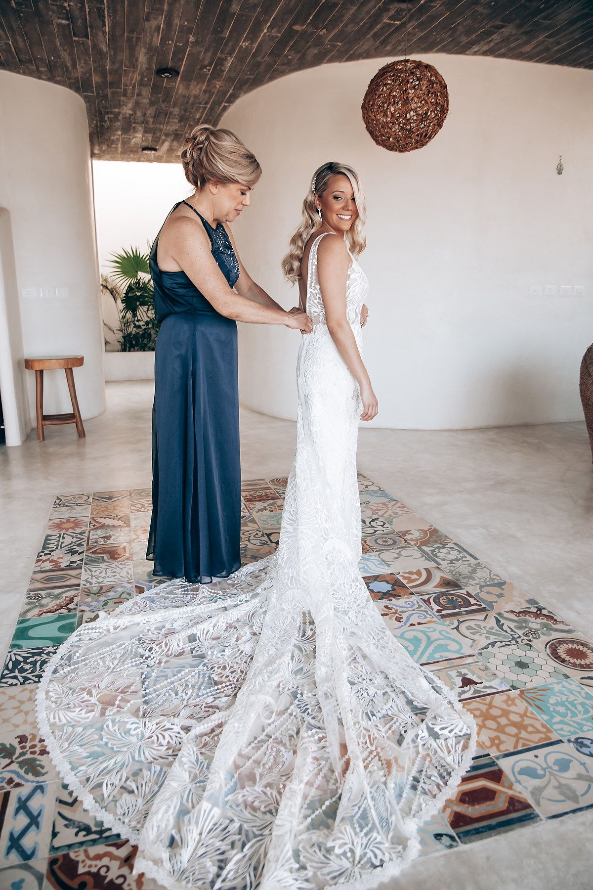Elegant white lace wedding dress with intricate details displayed on colorful patterned floor tiles.