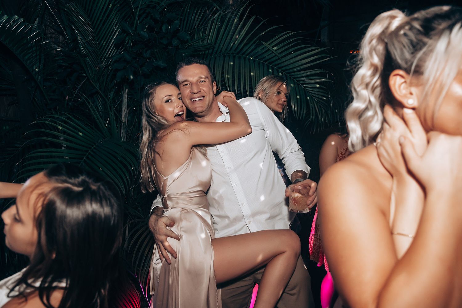 Wedding guests dancing and celebrating at reception with intimate lighting and festive atmosphere.