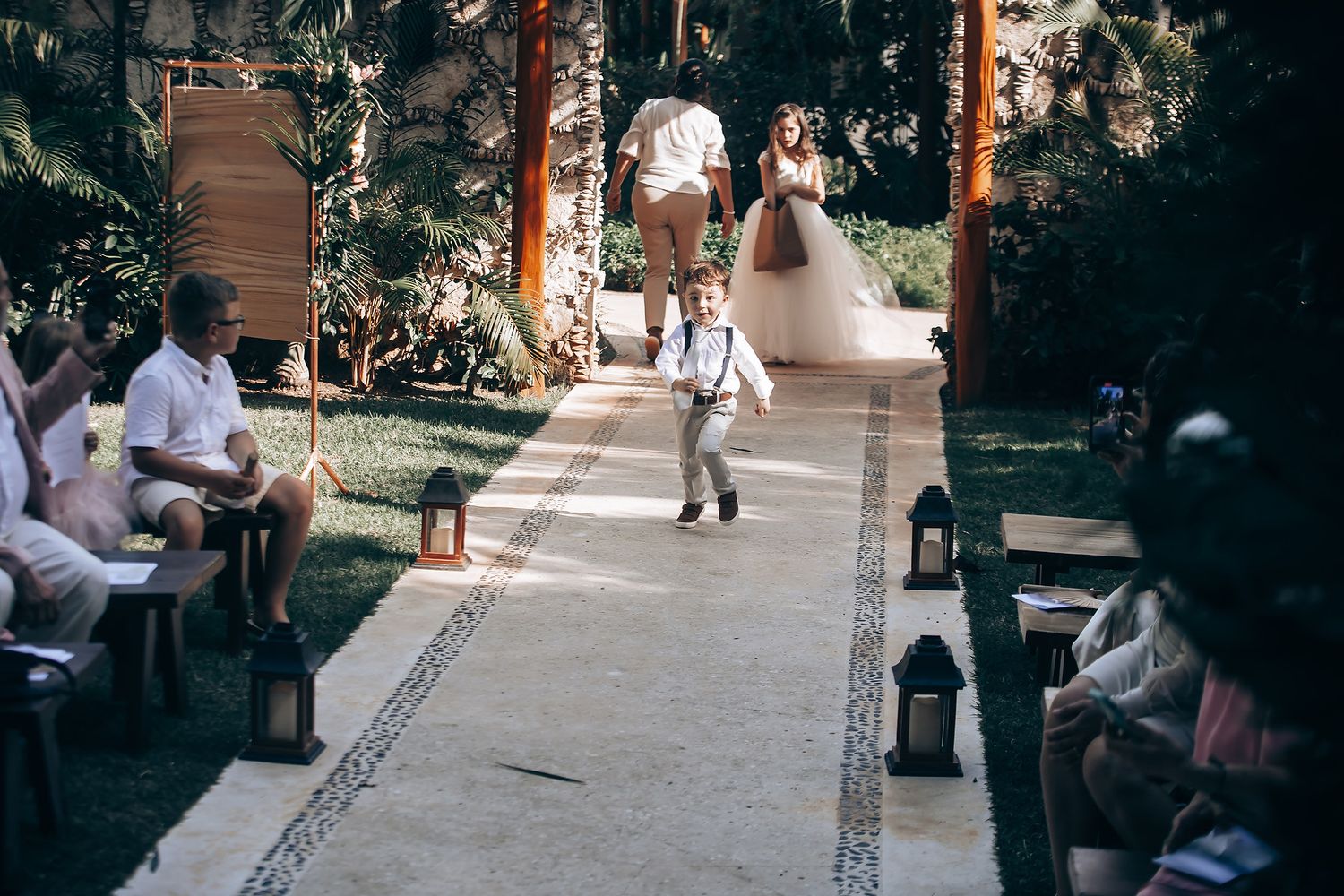 Wedding guests celebrate during an outdoor reception with string lights and palm trees at dusk.