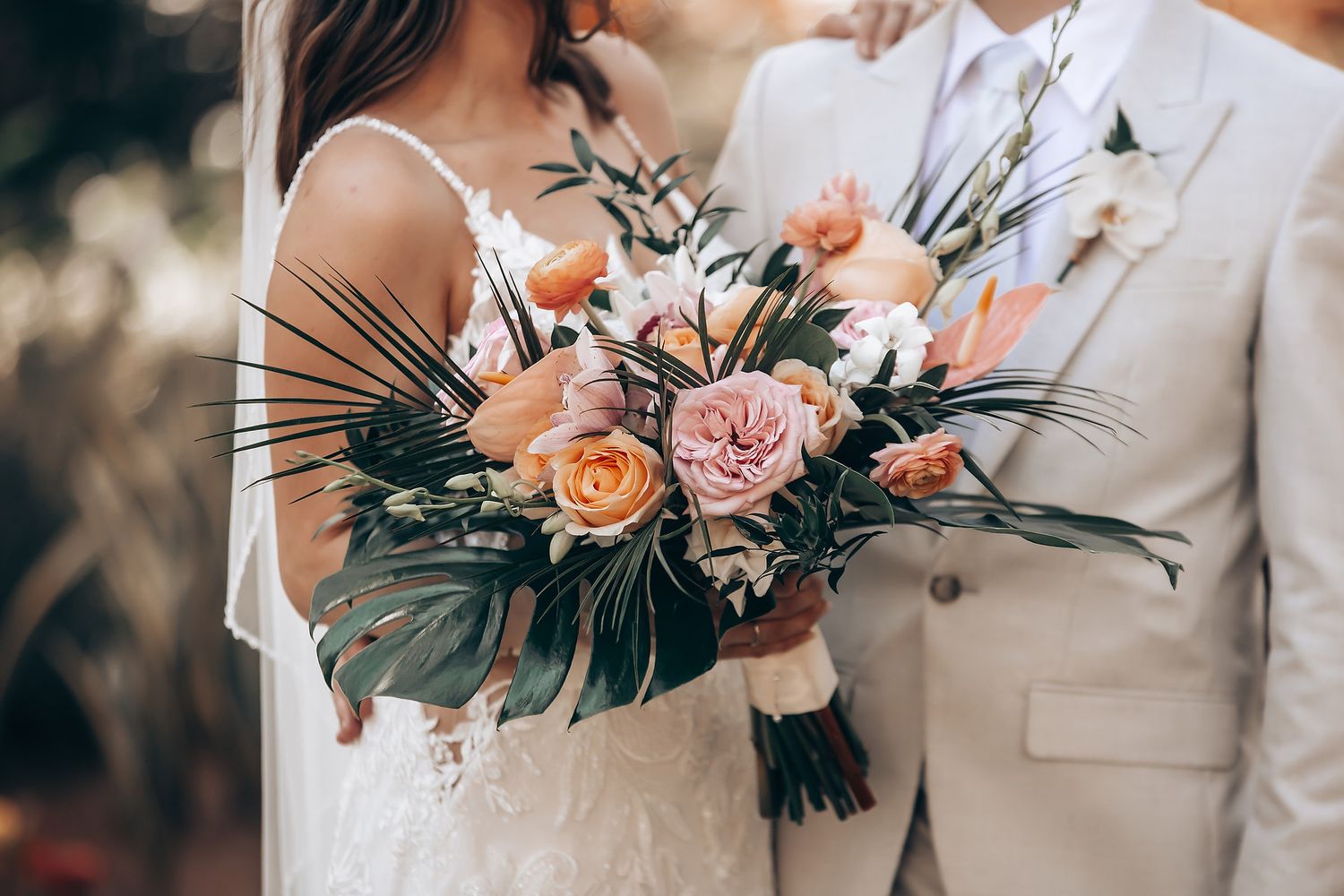 Romantic wedding bouquet featuring pink roses and tropical greenery.