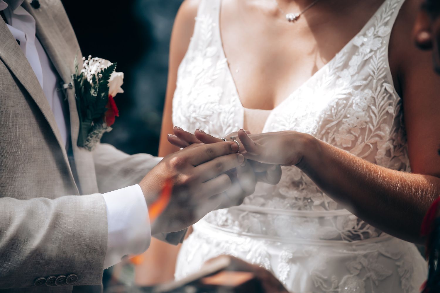 Close-up of wedding ring exchange showing detailed lace dress and formal attire.