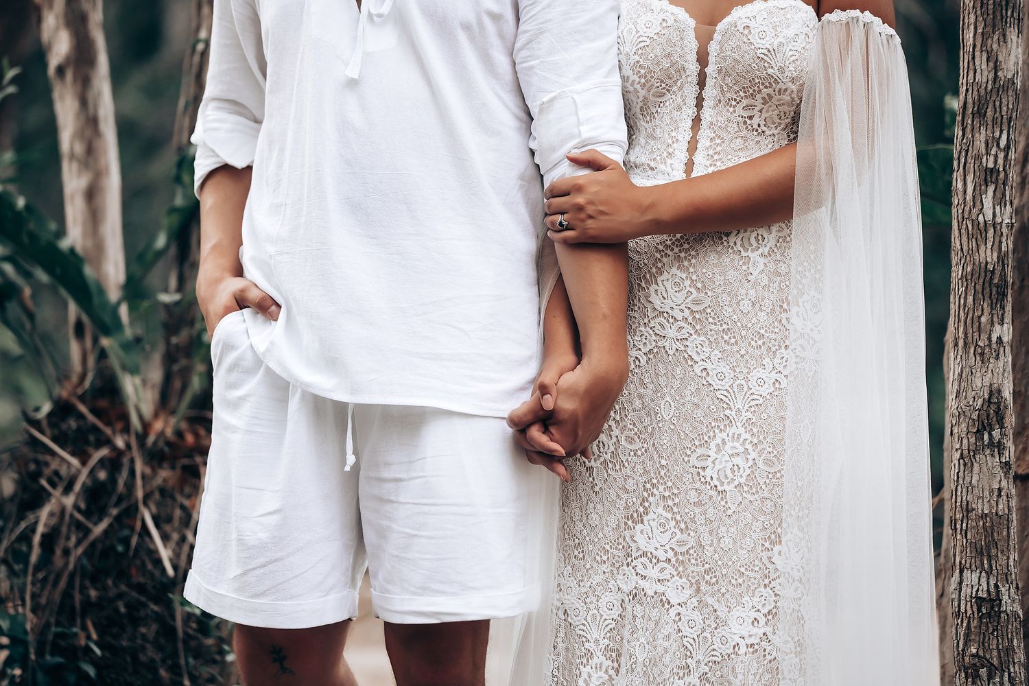 Couple in white attire sharing an intimate moment during outdoor wedding photoshoot with rustic wooden fence backdrop.