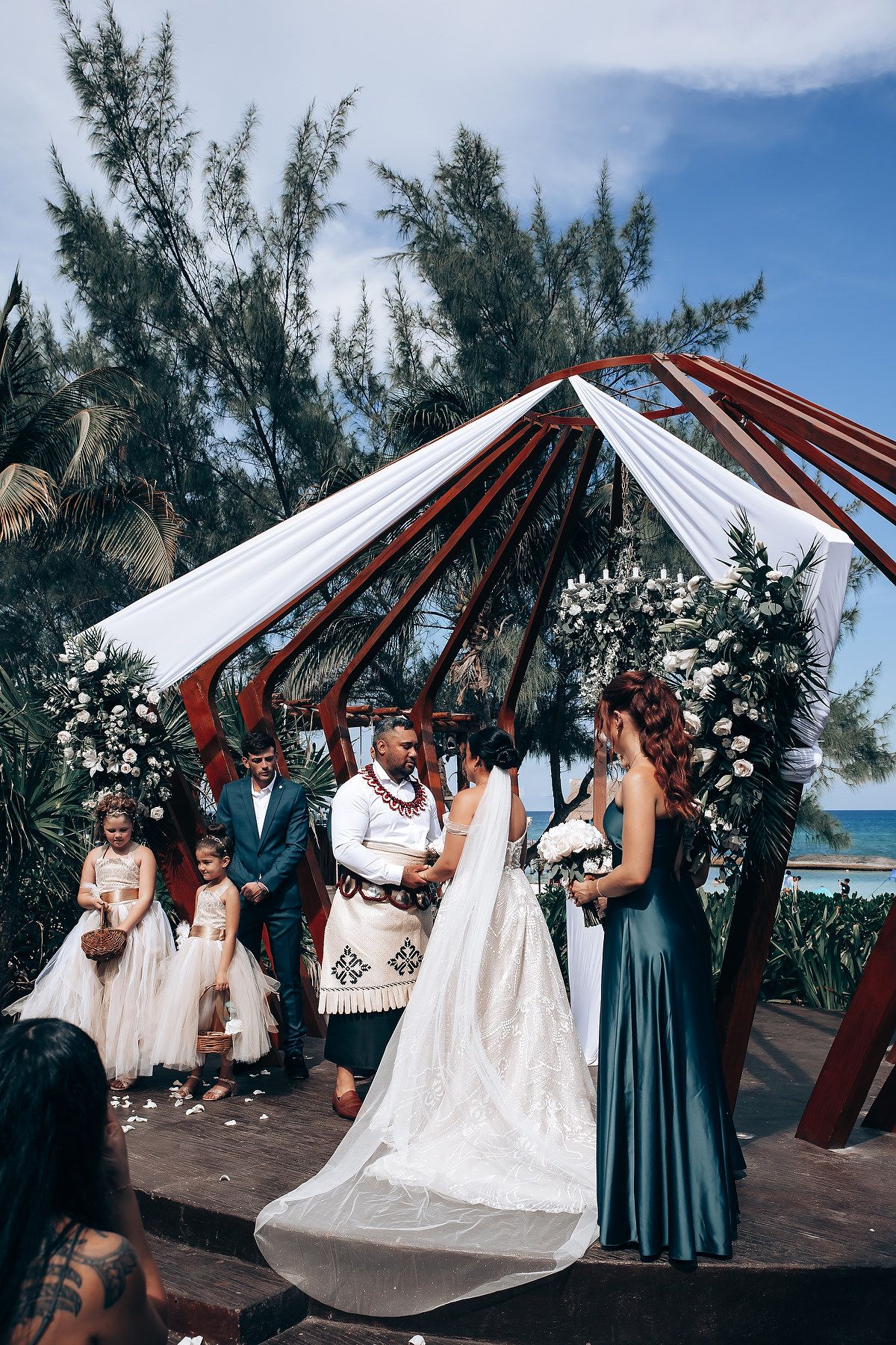 Beachside wedding ceremony under a white canopy with bridesmaids in teal dresses.