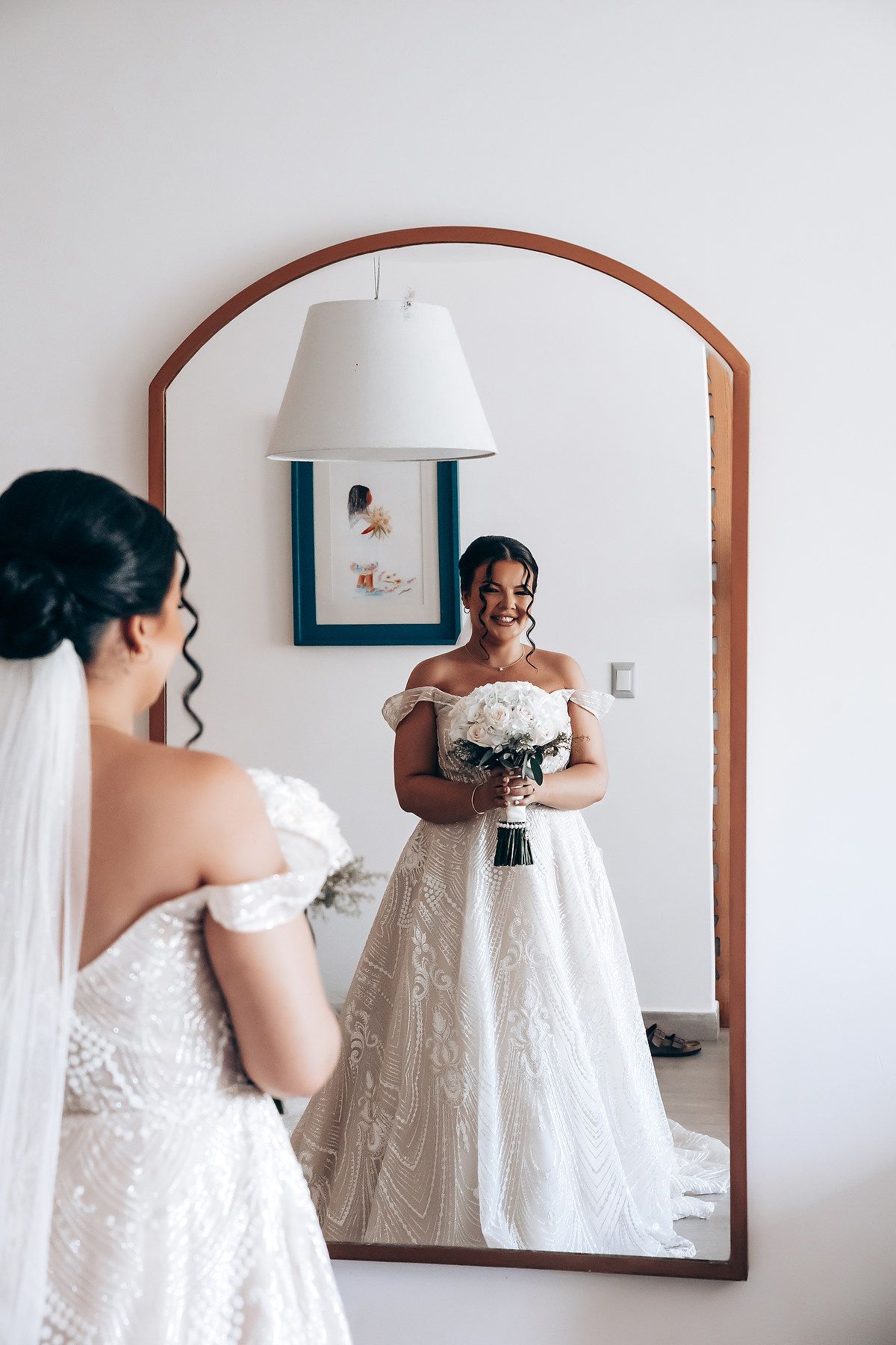 Mirror reflections showing wedding dress preparations in a bright white room.
