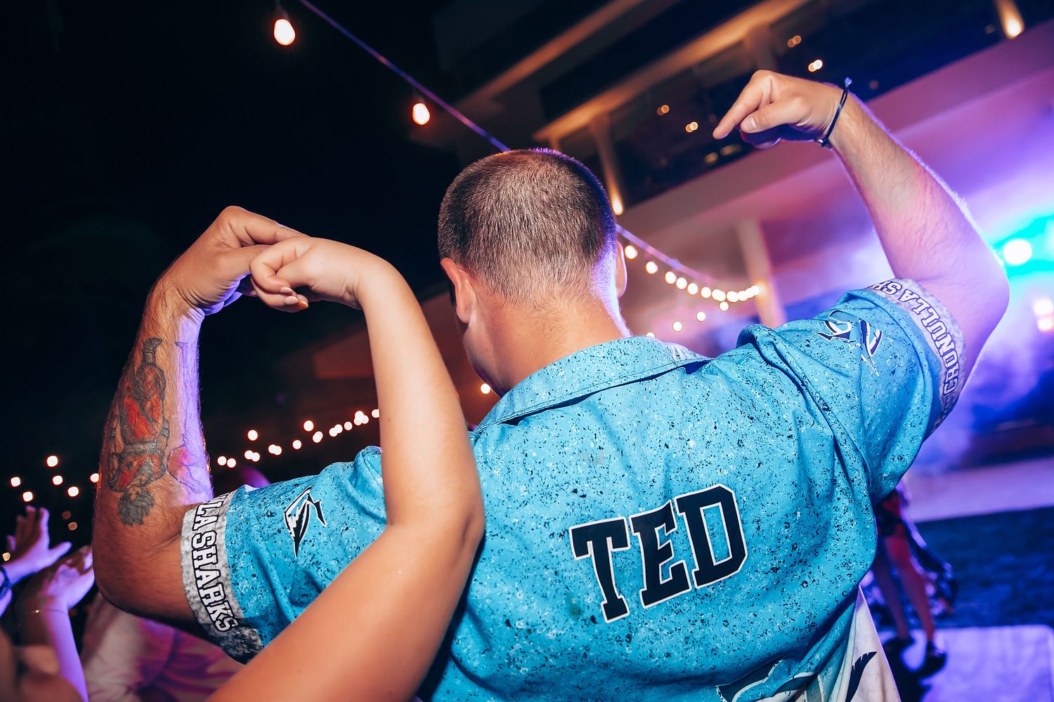 Party guests dancing under colorful lights at wedding reception.