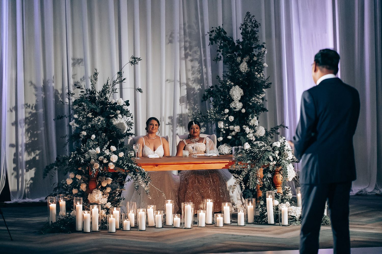 Romantic wedding reception setup with candlelight and floral arrangements framing a sweetheart table.