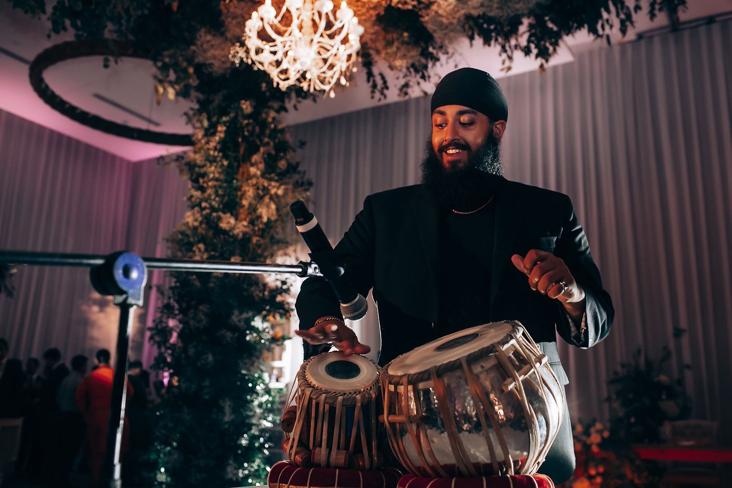 A musician plays the drums under an elegant chandelier at an indoor event venue.