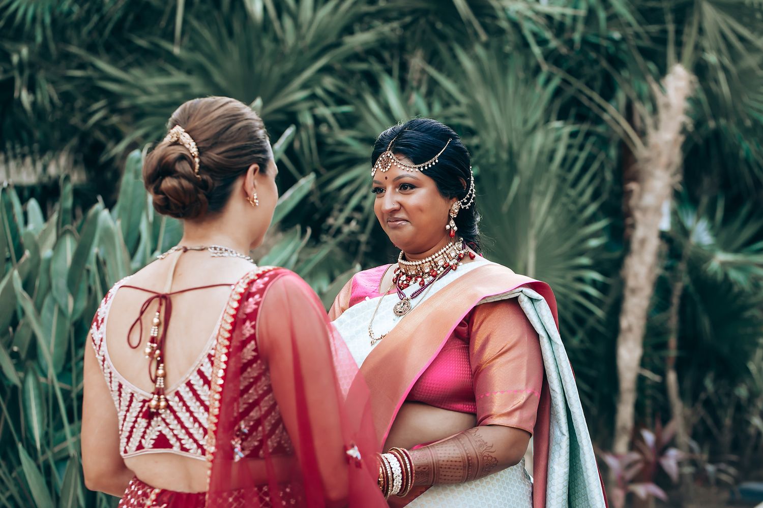 Wedding party members in red and pink traditional Indian attire gathered outdoors.